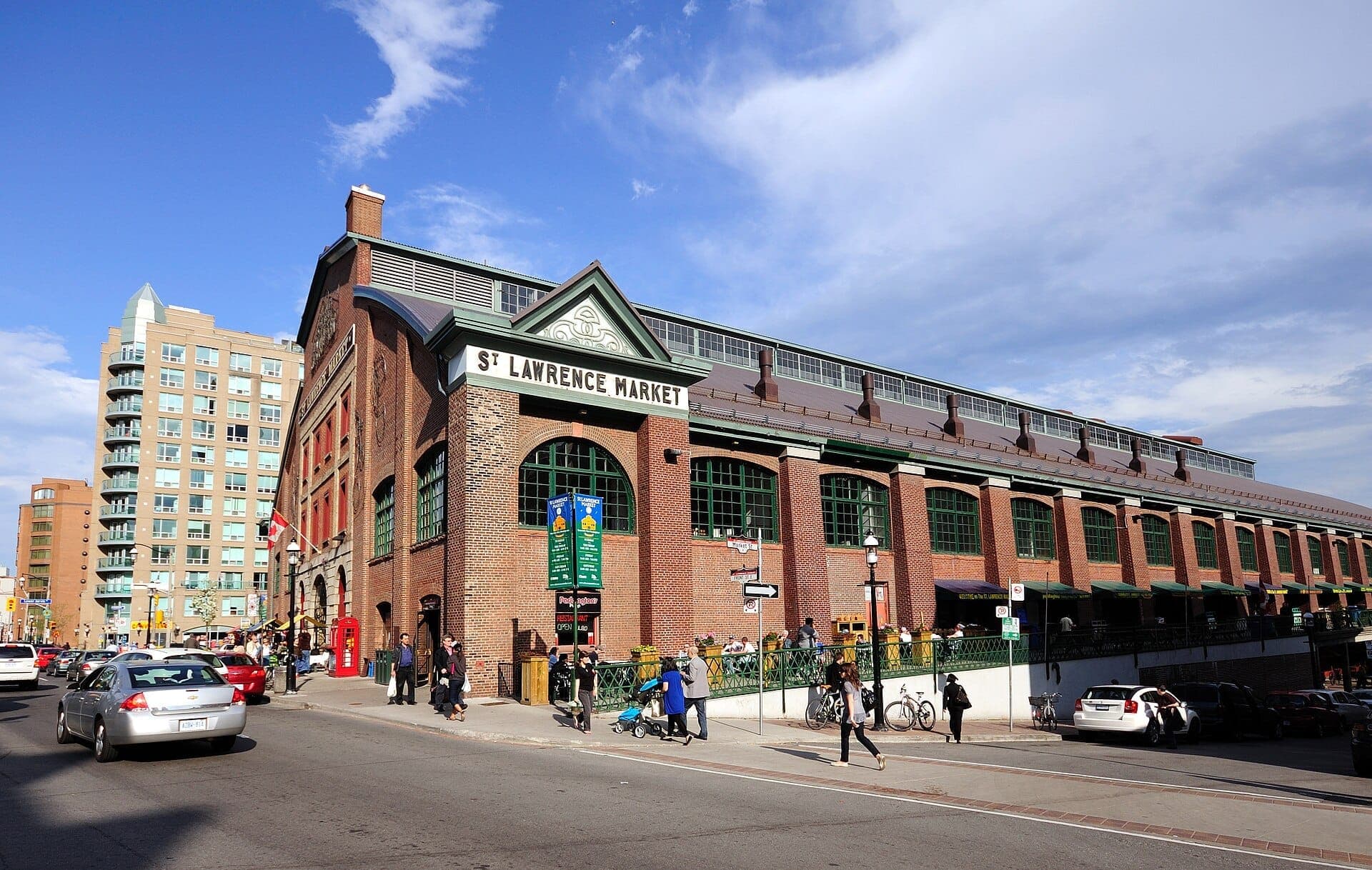 Edificio dello St. Lawrence Market a Toronto con esterno in mattoni rossi, grandi finestre verdi e persone che camminano in una giornata di sole.