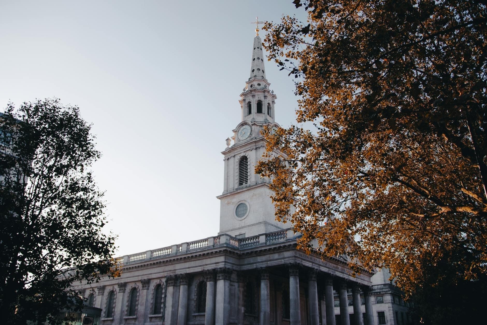 La chiesa di St Martin-in-the-Fields a Londra con il suo alto campanile, incorniciata da alberi autunnali sotto un cielo sereno.