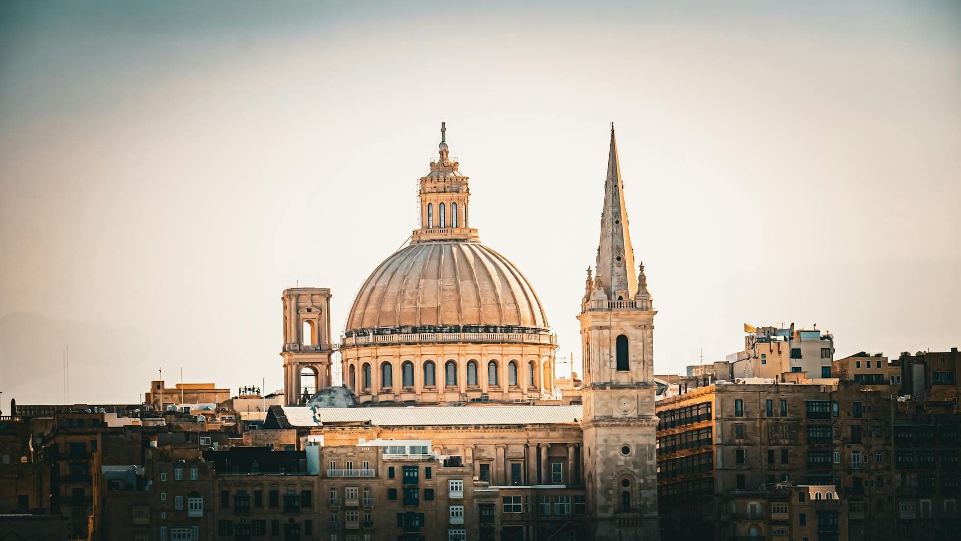 Große barocke Kuppel und Turm der St. Paul's Cathedral in Mdina, Malta, die sich über die honigfarbenen Stadtgebäude unter klarem Morgenlicht erheben.