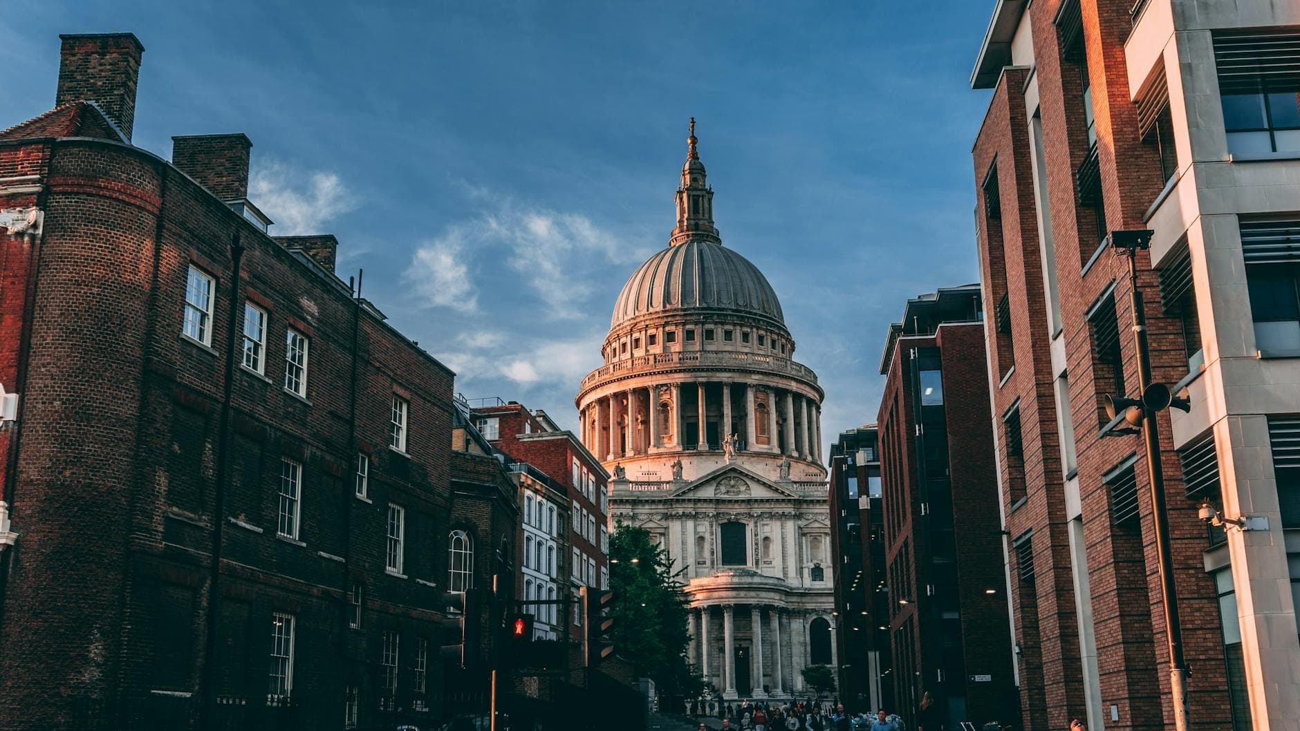 St Paul's Cathedral, eingerahmt von historischen und modernen Gebäuden einer Londoner Straße bei Sonnenuntergang – die ikonische Kuppel unter einem dramatisch blauen Himmel.