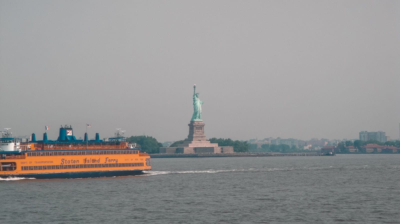 เรือ Staten Island Ferry สีส้มกำลังล่องข้ามอ่าวนิวยอร์ก เทพีเสรีภาพเห็นอยู่ไกล ๆ ในวันที่หมอกลงจาง ๆ