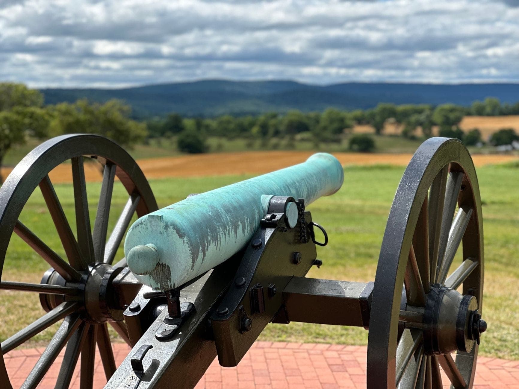 Historic Civil War cannon at Stones River National Battlefield with rolling green fields and distant hills under a cloudy sky.