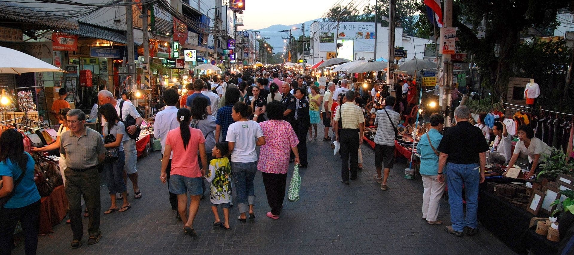 Menschenmassen schlendern entlang der Chiang Mai Sunday Walking Street auf der Ratchadamnoen Road und stöbern in hell erleuchteten Marktständen und lokalen Geschäften in der Abenddämmerung.
