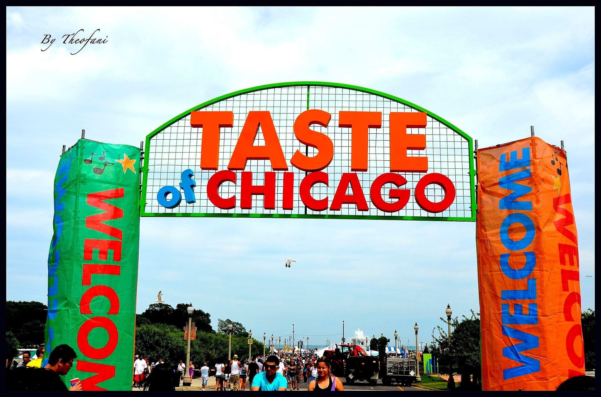 Large Taste of Chicago sign welcomes crowds at Grant Park under a cloudy blue sky, with colorful banners and festivalgoers in the foreground.