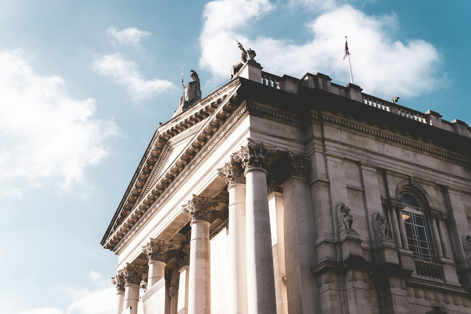 La façade néoclassique en pierre de la Tate Britain, avec ses colonnes et ses statues se détachant sur un ciel bleu vif parsemé de nuages légers.