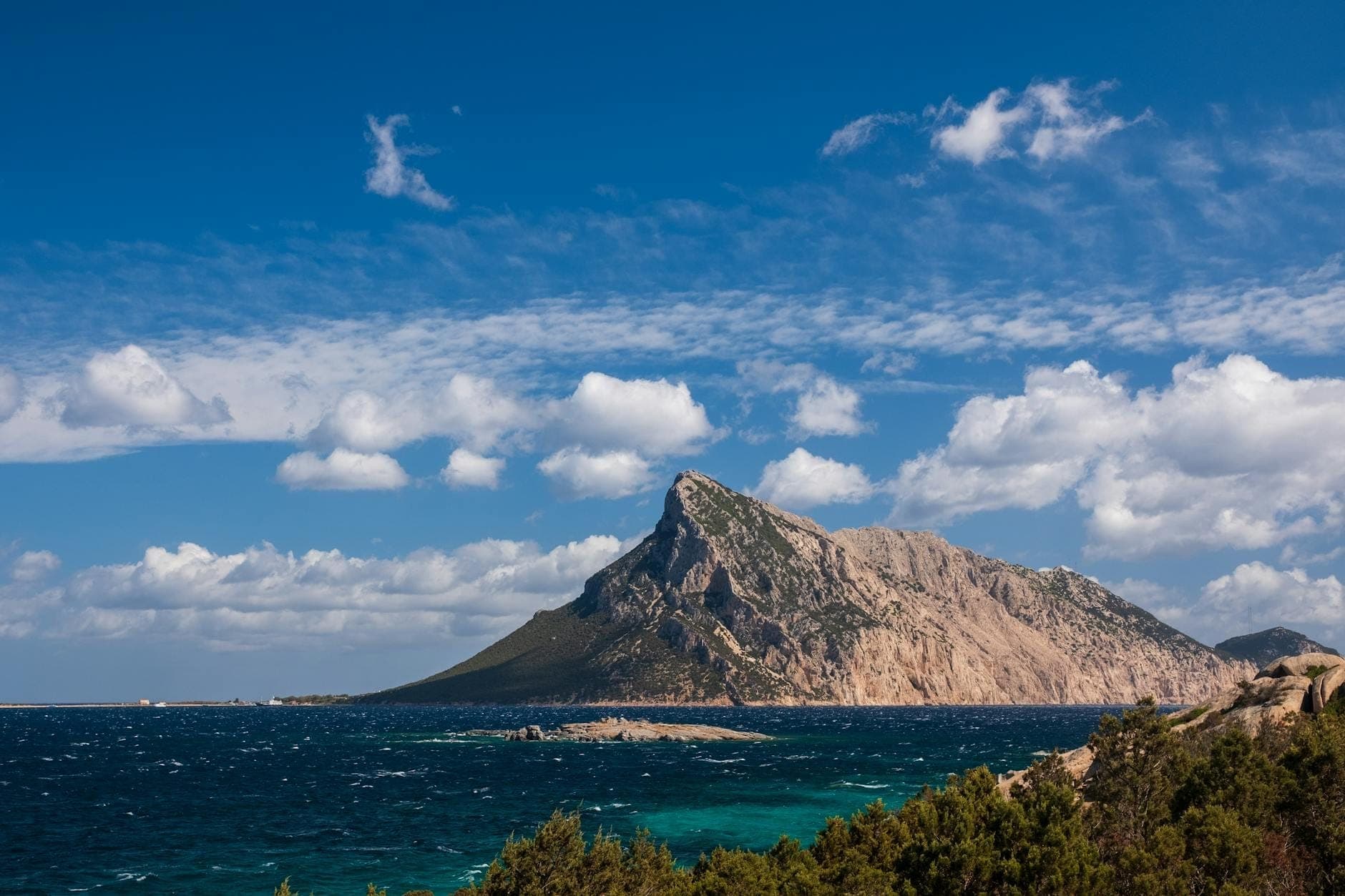 La dramática isla calcárea de Isola Tavolara emerge abruptamente del profundo azul del mar Tirreno, con nubes dispersas y una costa salvaje en primer plano.