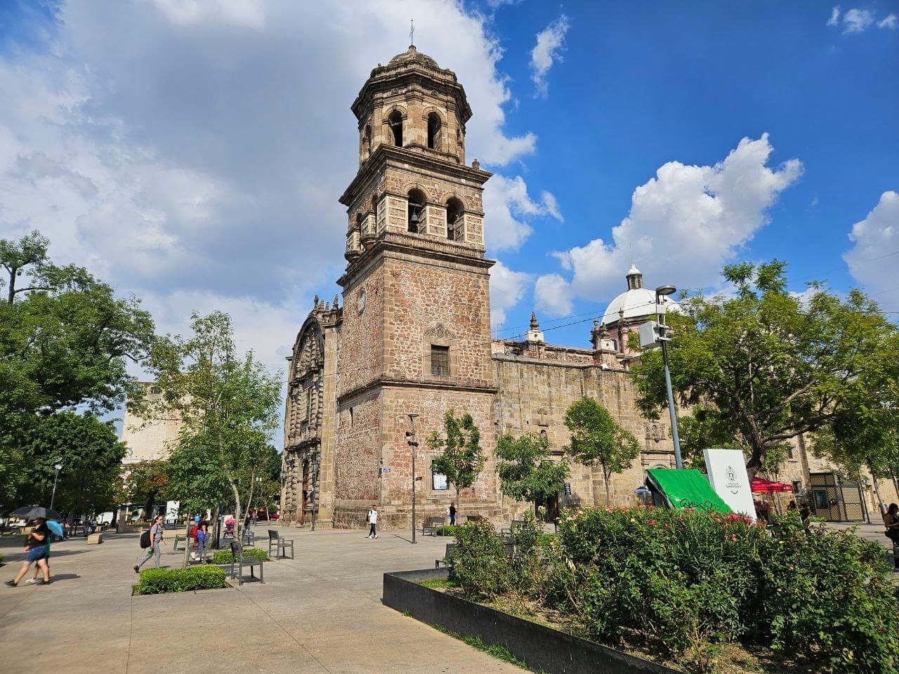 Templo de San Francisco de Asís ในเมือง Guadalajara ตั้งตระหง่านพร้อมหอคอยหินประวัติศาสตร์ ล้อมรอบด้วยต้นไม้เขียวขจีและนักท่องเที่ยวในวันที่แดดสดใส