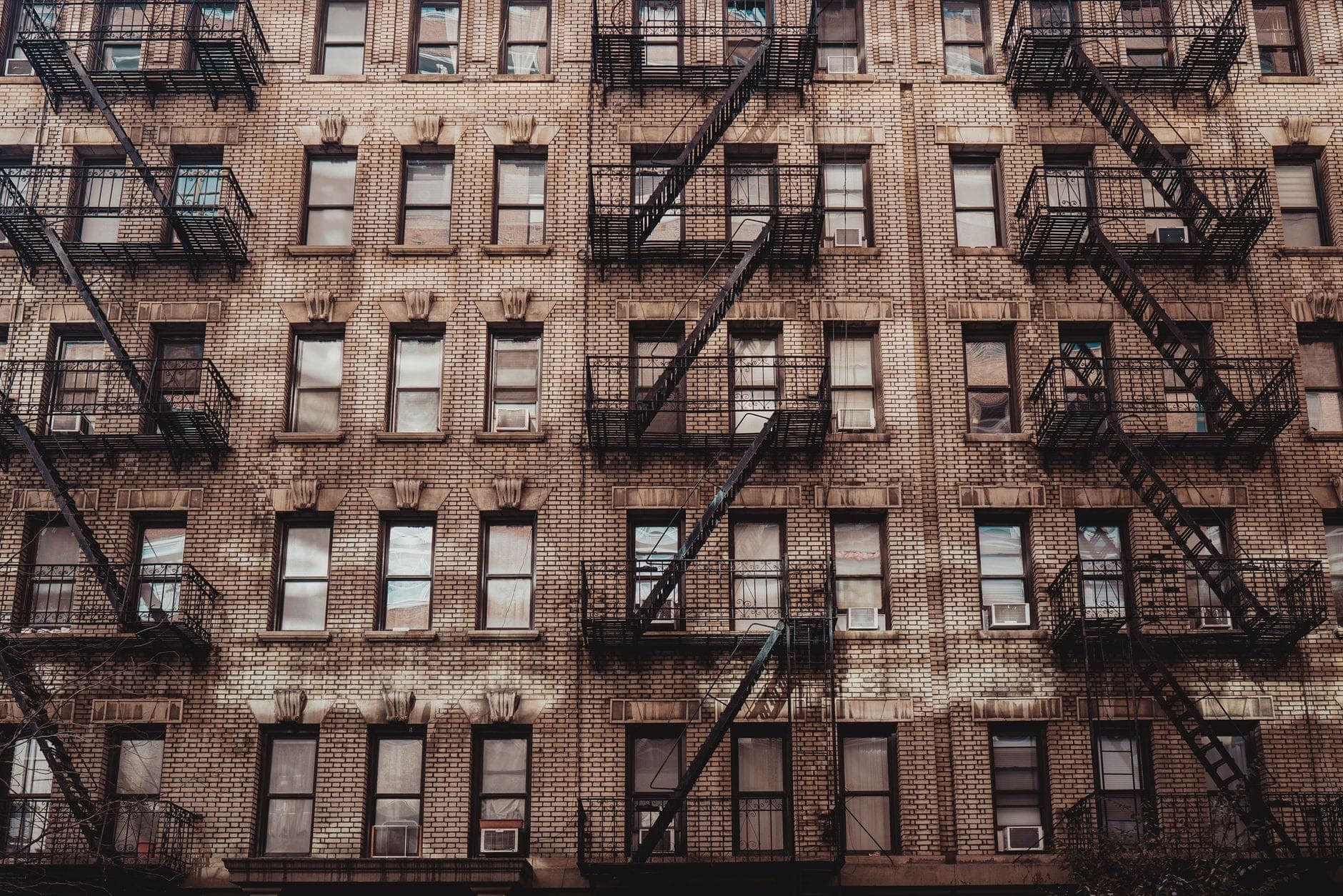 อาคาร Tenement ในมหานครนิวยอร์กแบบคลาสสิก มีหน้าต่างเรียงหลายแถวกับบันไดหนีไฟเหล็กสีดำ โชว์สถาปัตยกรรมยุคเก่าในแสงแดดพอดี