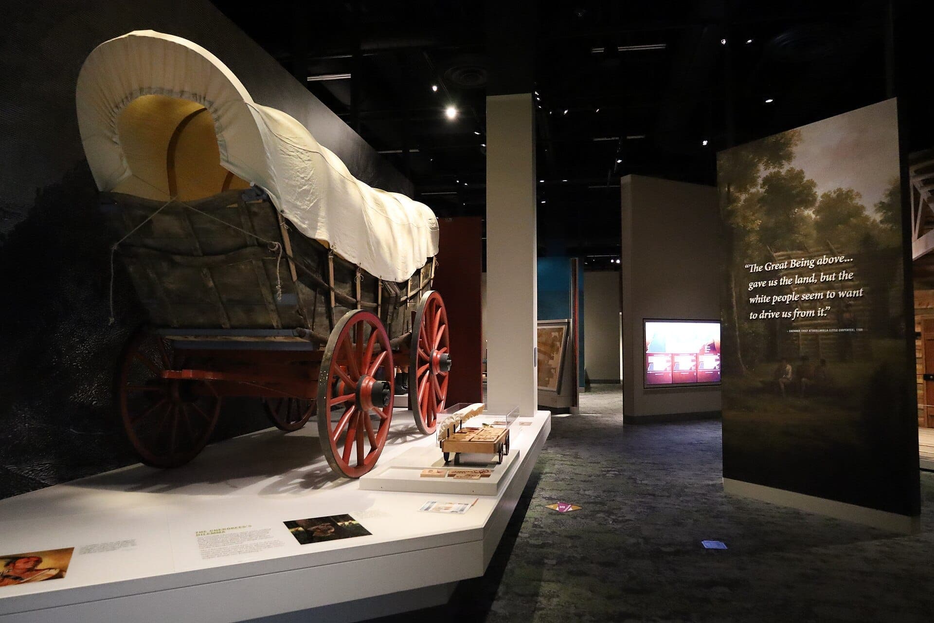 Covered wagon display at the Tennessee State Museum, with red wooden wheels and educational panels in a dimly lit exhibition space.