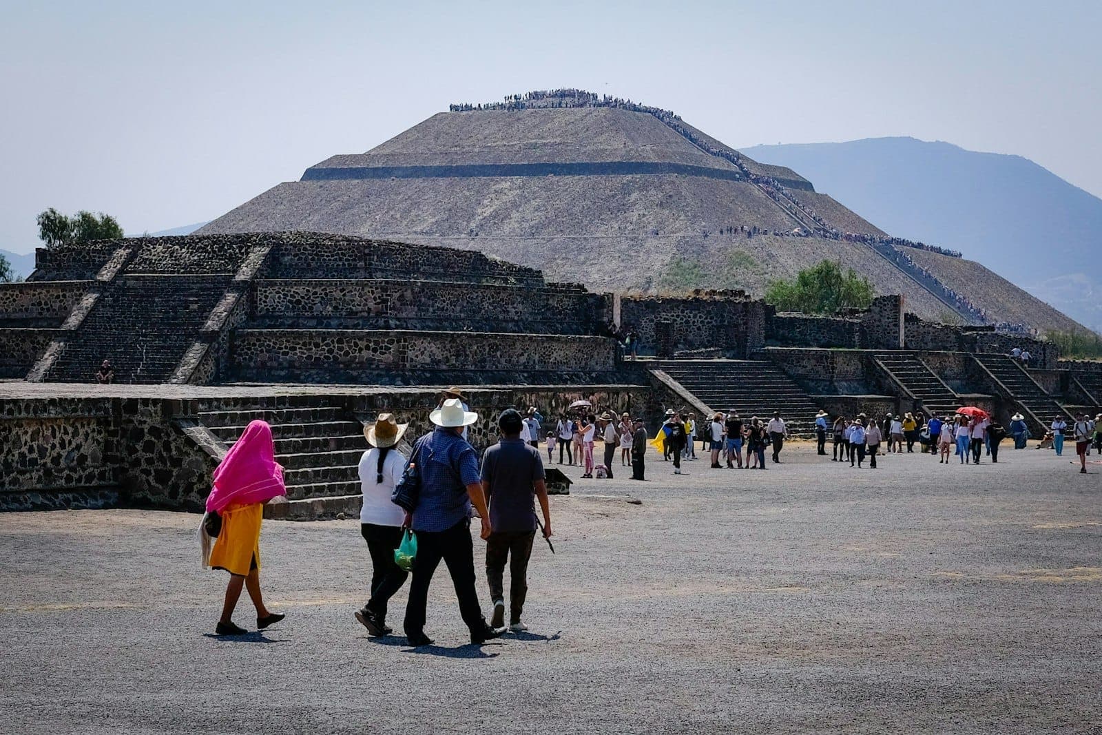 Vue de la Pyramide du Soleil de Teotihuacán avec des foules de visiteurs marchant le long de l'Avenue des Morts sous un ciel dégagé