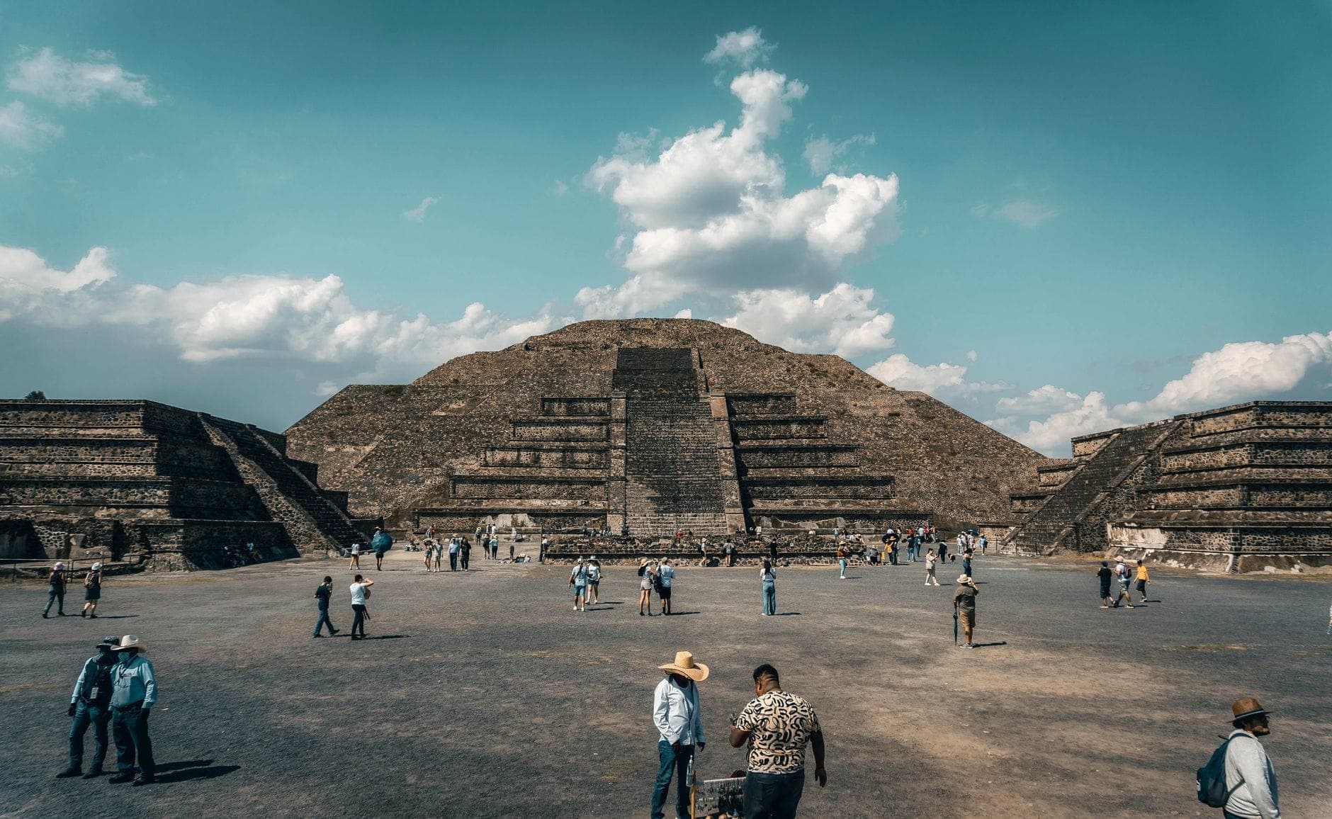 Vue panoramique de la Pyramide du Soleil à Teotihuacán avec de nombreux visiteurs se promenant et explorant l'ancienne place sous un ciel bleu.
