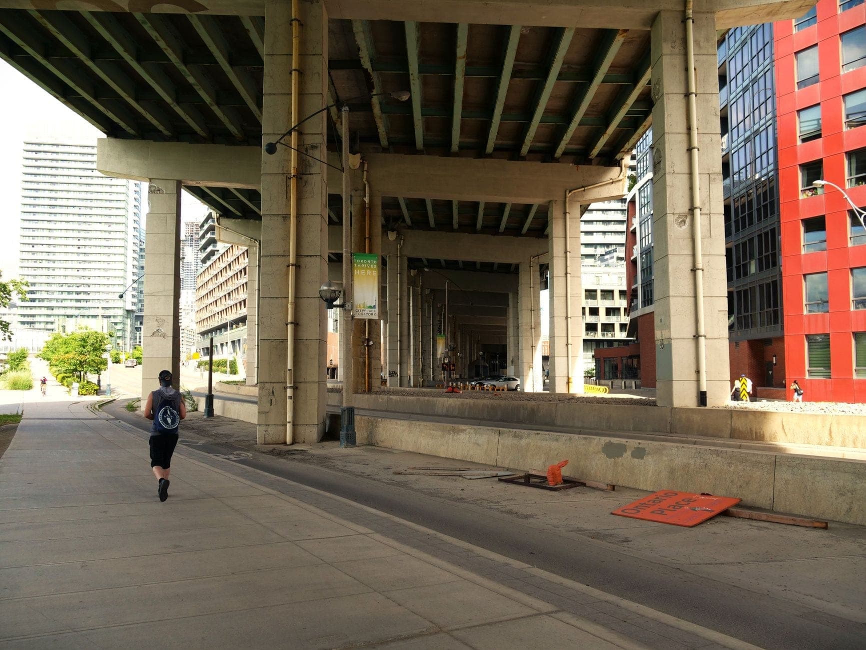 Una visione ampia sotto il Gardiner Expressway a Toronto, con il percorso pedonale e ciclabile, un runner e moderni edifici su entrambi i lati.