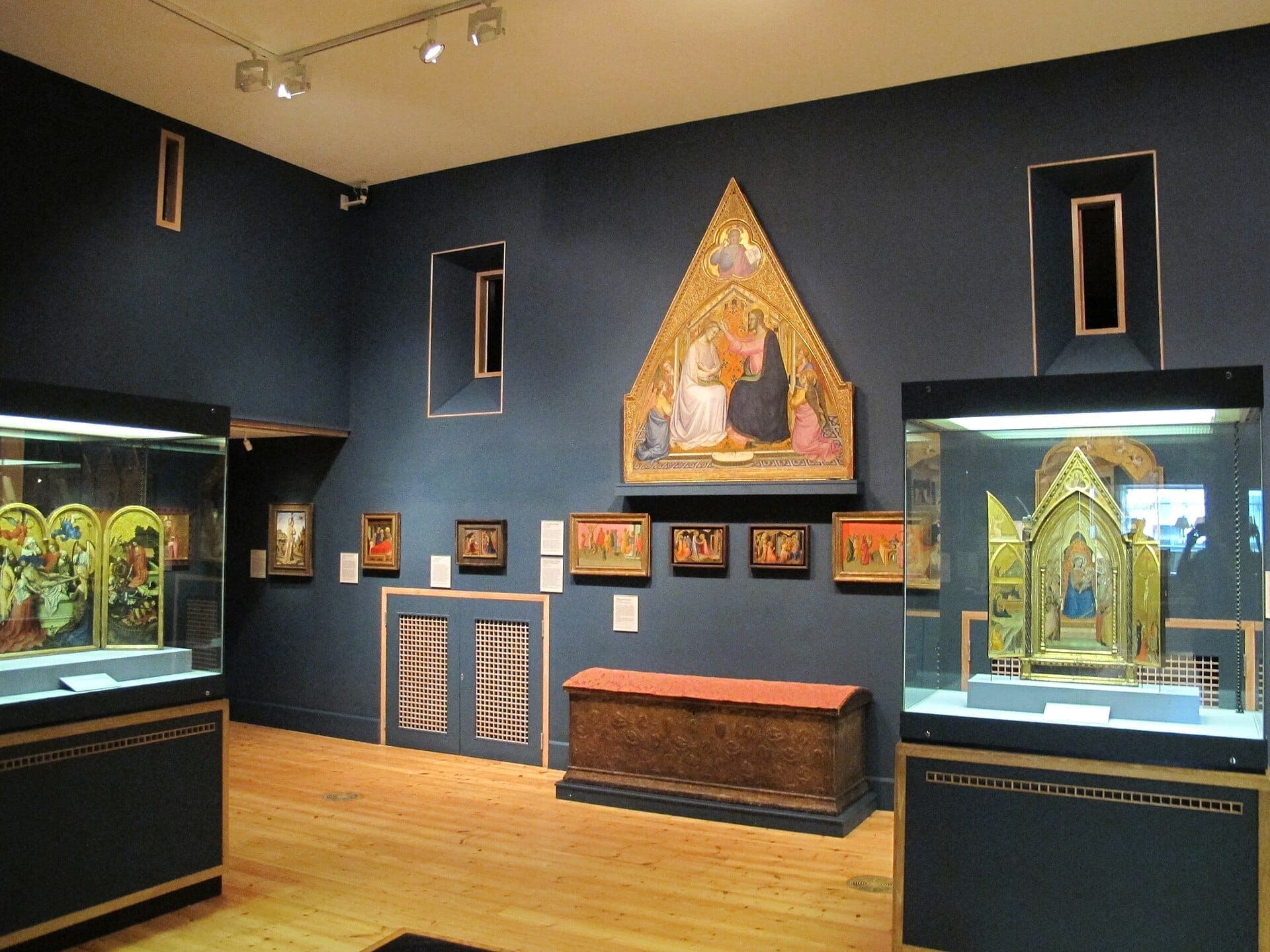 Galerieraum in The Courtauld Gallery mit beleuchteten mittelalterlichen Altarbildern, religiösen Gemälden und verzierten Holzböden unter gedämpfter Ausstellungsbeleuchtung.