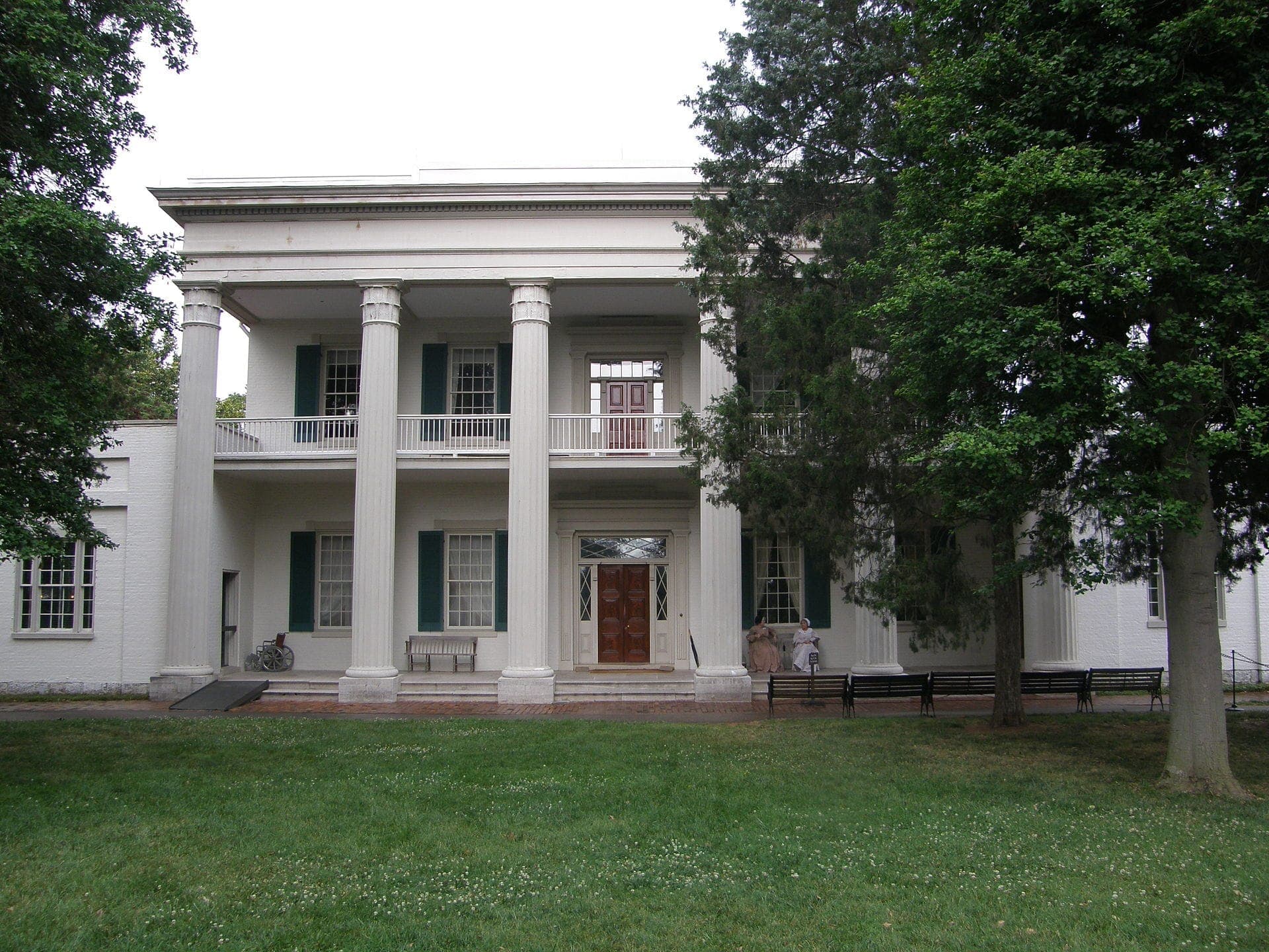 Vorderansicht der Hermitage-Herrenhauses von Andrew Jackson mit imposanten weißen Säulen, grünen Fensterläden und umgeben von üppigen Bäumen und Rasen an einem bewölkten Tag.