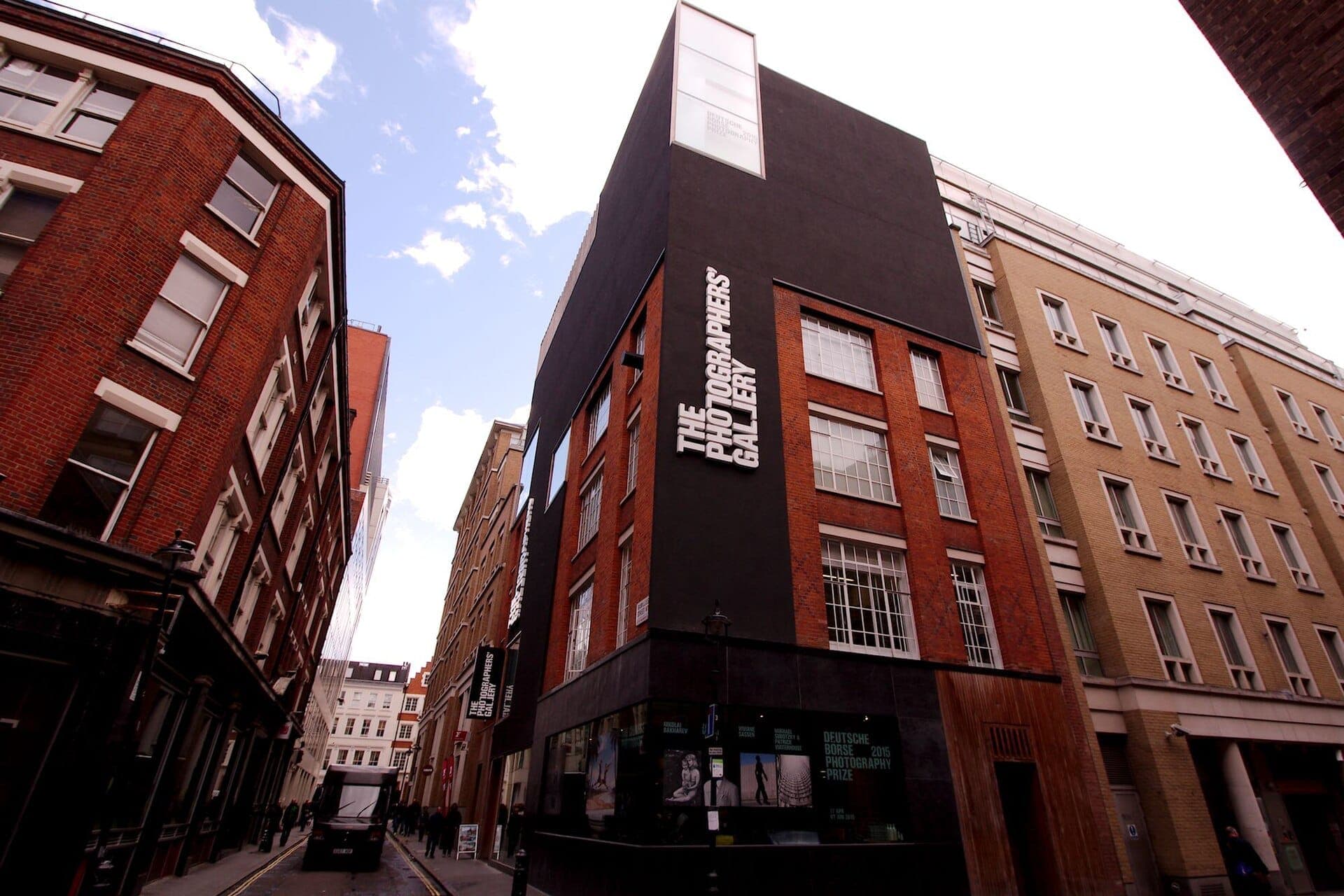 Das Gebäude der The Photographers' Gallery in der Ramillies Street in London, mit rotem Backstein und schwarzer Verkleidung, umgeben von historischer Stadtarchitektur.