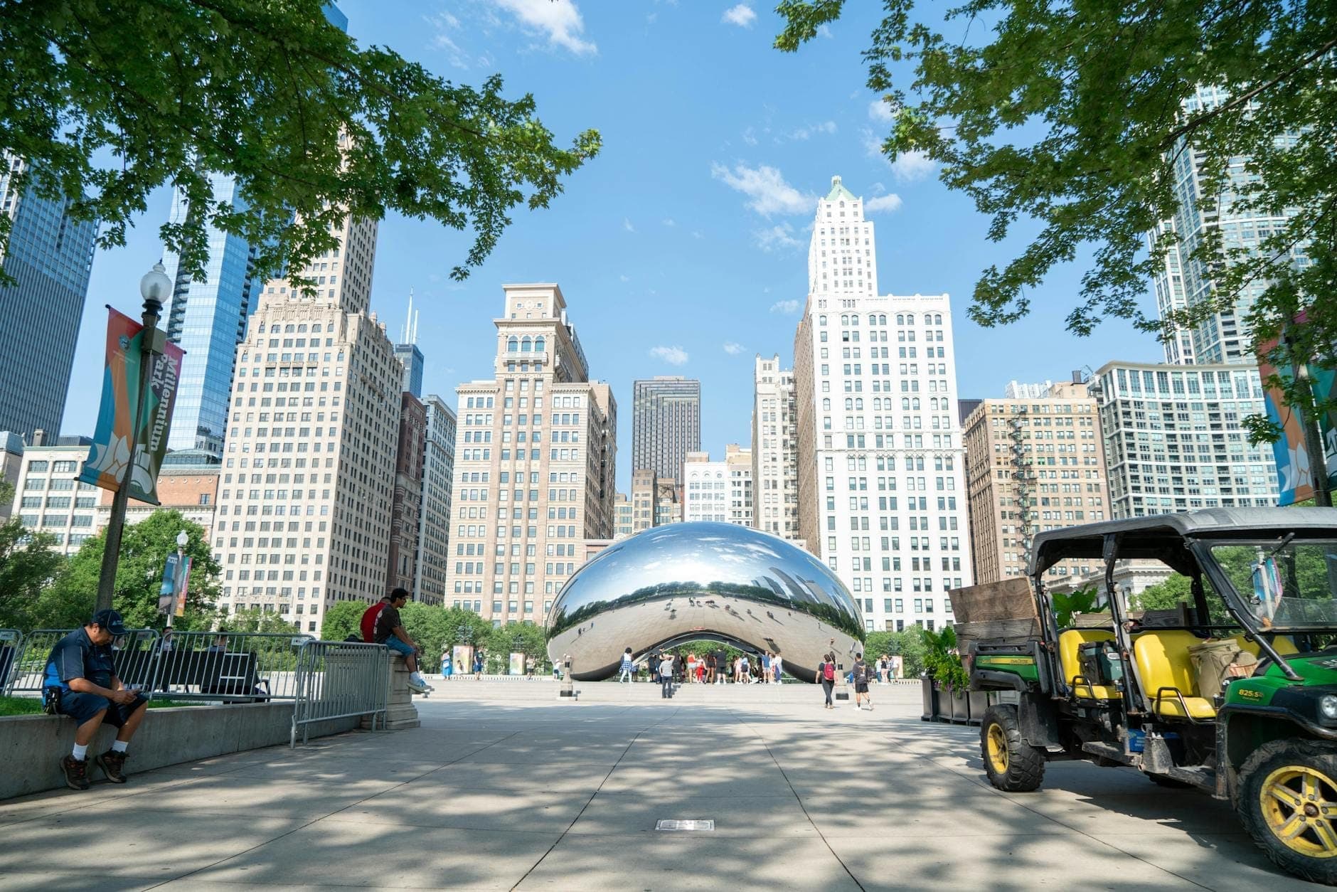 Cloud Gate sculpture in Millennium Park with surrounding skyscrapers and people walking on a sunny day in downtown Chicago.