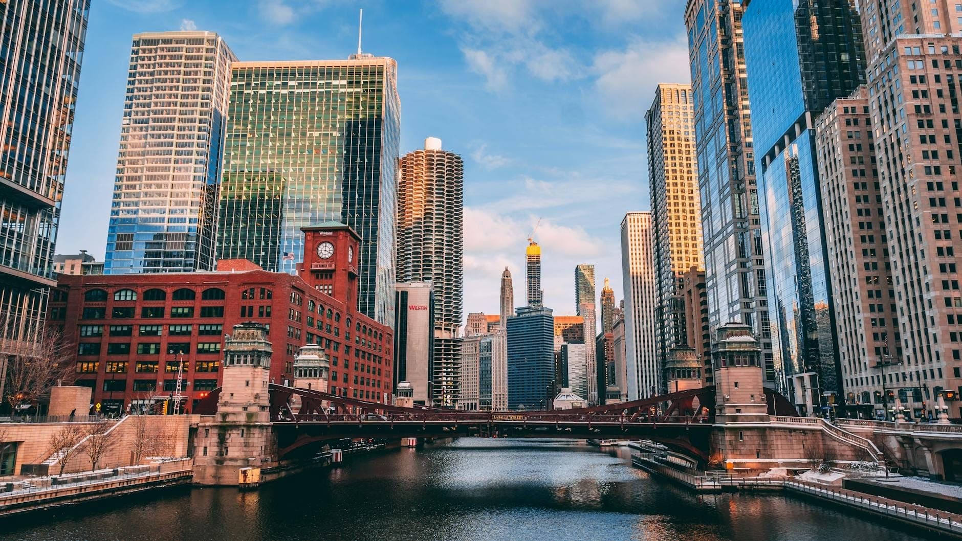 Stunning view of downtown Chicago skyline at sunset with skyscrapers reflecting in the river and a historic bridge in the foreground.