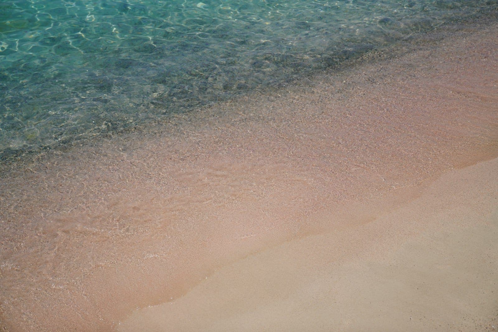 Agua clara y turquesa que se encuentra con una playa de arena de un característico tono rosado, una vista clásica de Elafonissi Beach en Creta.