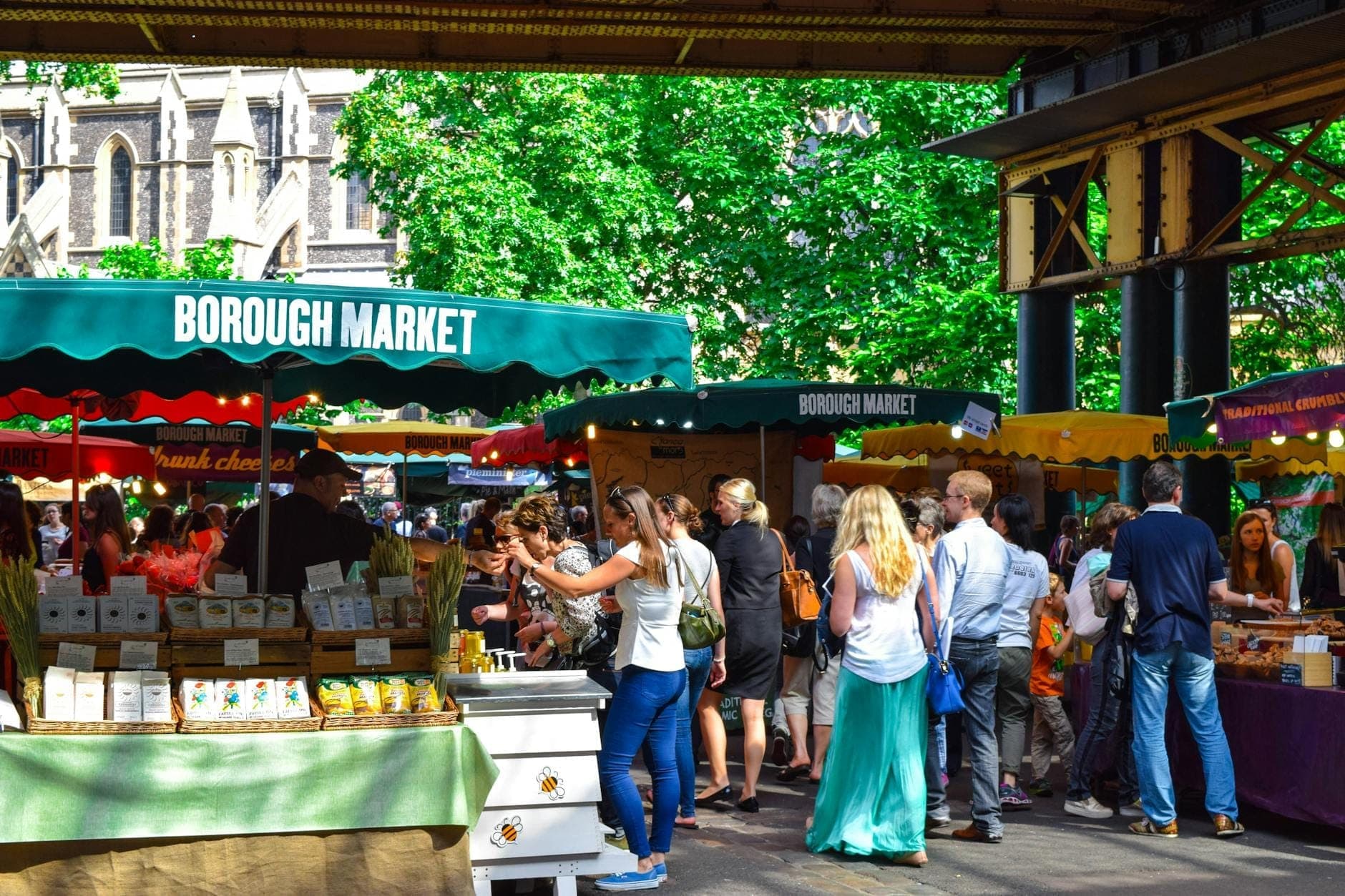 Multitudes curioseando puestos de comida bajo toldos verdes con el letrero Borough Market en un animado entorno al aire libre con frutas, verduras y productos visibles.
