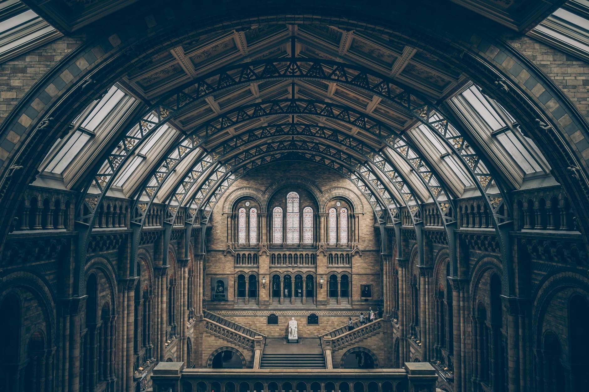 Vista amplia del gran salón con arcos en el interior del Museo de Historia Natural de Londres, con ornamentación de piedra y personas en el balcón.