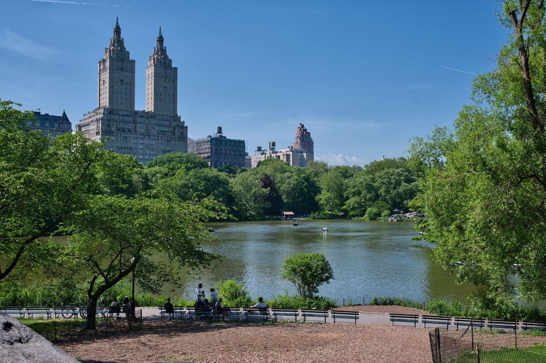 วิวสวยงามของ Central Park พร้อมต้นไม้ ทะเลสาบ ม้านั่ง และตึกสูงของ New York City เป็นฉากหลังใต้ท้องฟ้าสีฟ้า