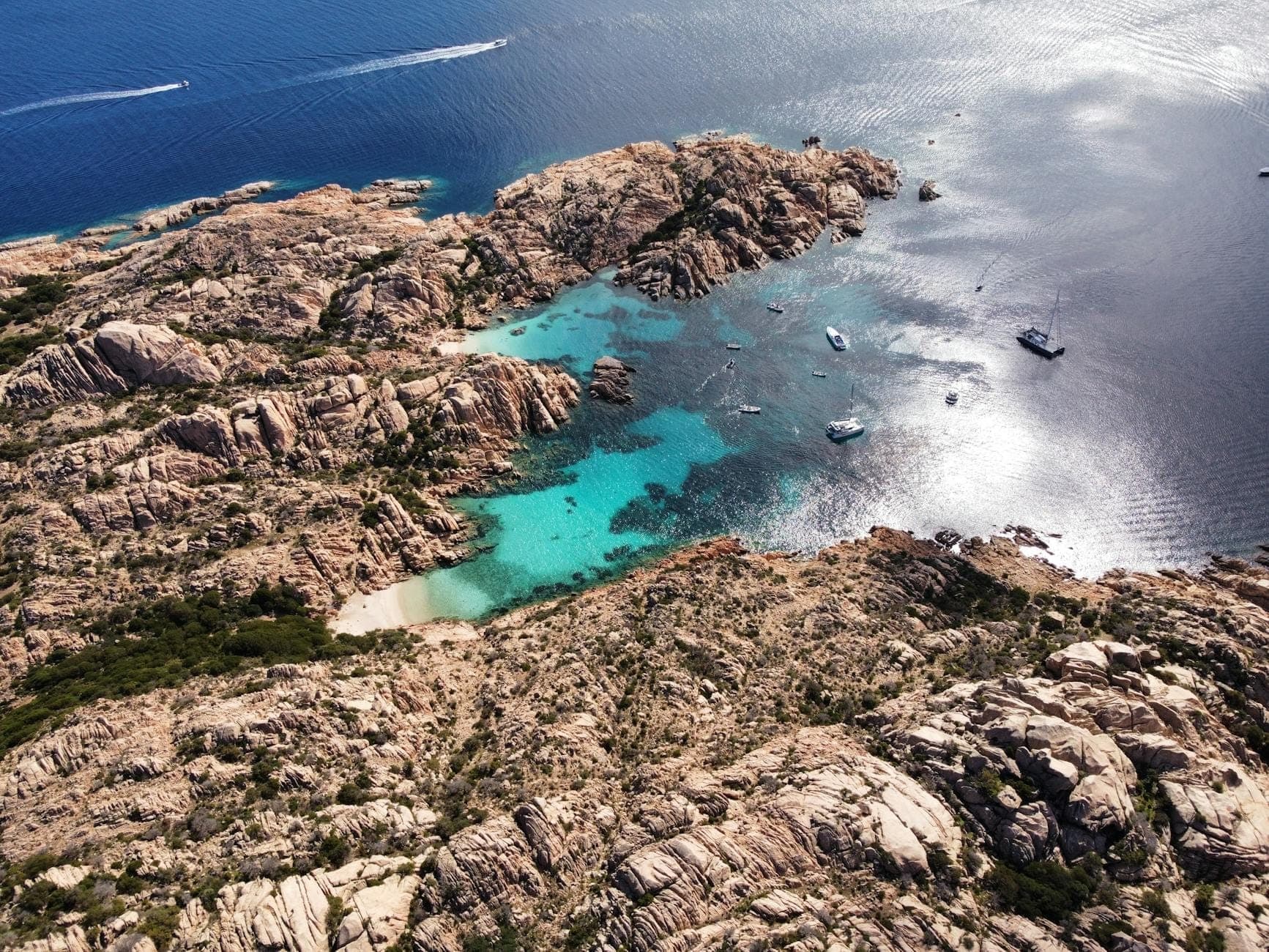 Vista aérea de una costa rocosa con calas de agua turquesa, pequeñas embarcaciones ancladas en aguas cristalinas y paisajes espectaculares en la costa de Cerdeña.