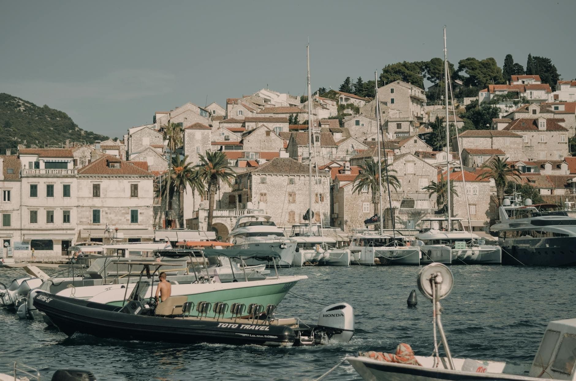 Scène de port avec des bateaux sur l'eau, des palmiers et des bâtiments de la ville sur la colline à Hvar, près de Split, en Croatie.