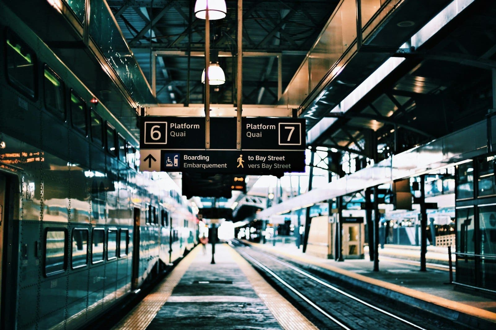 Toronto train station platforms with GO Transit trains, signage for platforms 6 and 7, and a passenger walking along the platform.