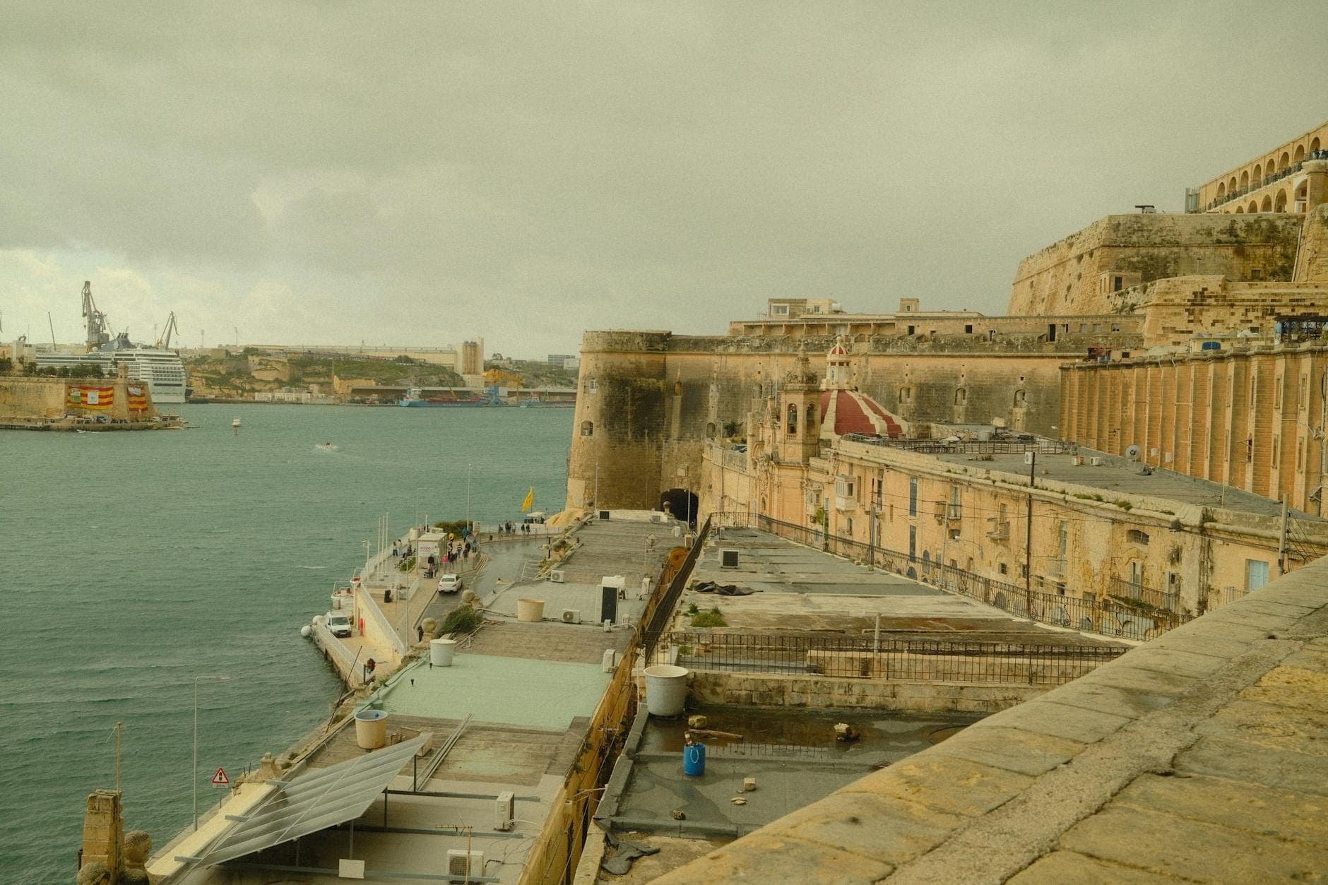 View of a large stone fortification on the waterfront in Valletta, Malta, with historic walls and buildings overlooking the harbor.