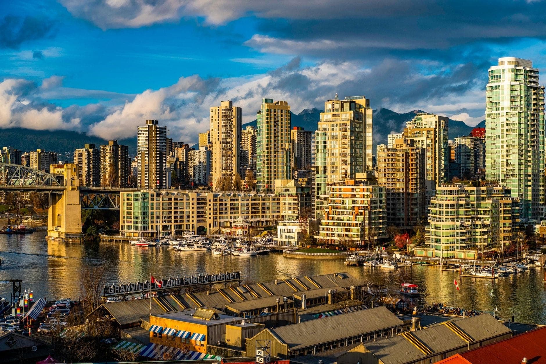 อาคารตลาดสาธารณะสีสันสดใสในเบื้องหน้ามองเห็น False Creek พร้อมเรือ ตึกระฟ้า และ Burrard Bridge ในเมืองแวนคูเวอร์ รัฐบริติชโคลัมเบีย