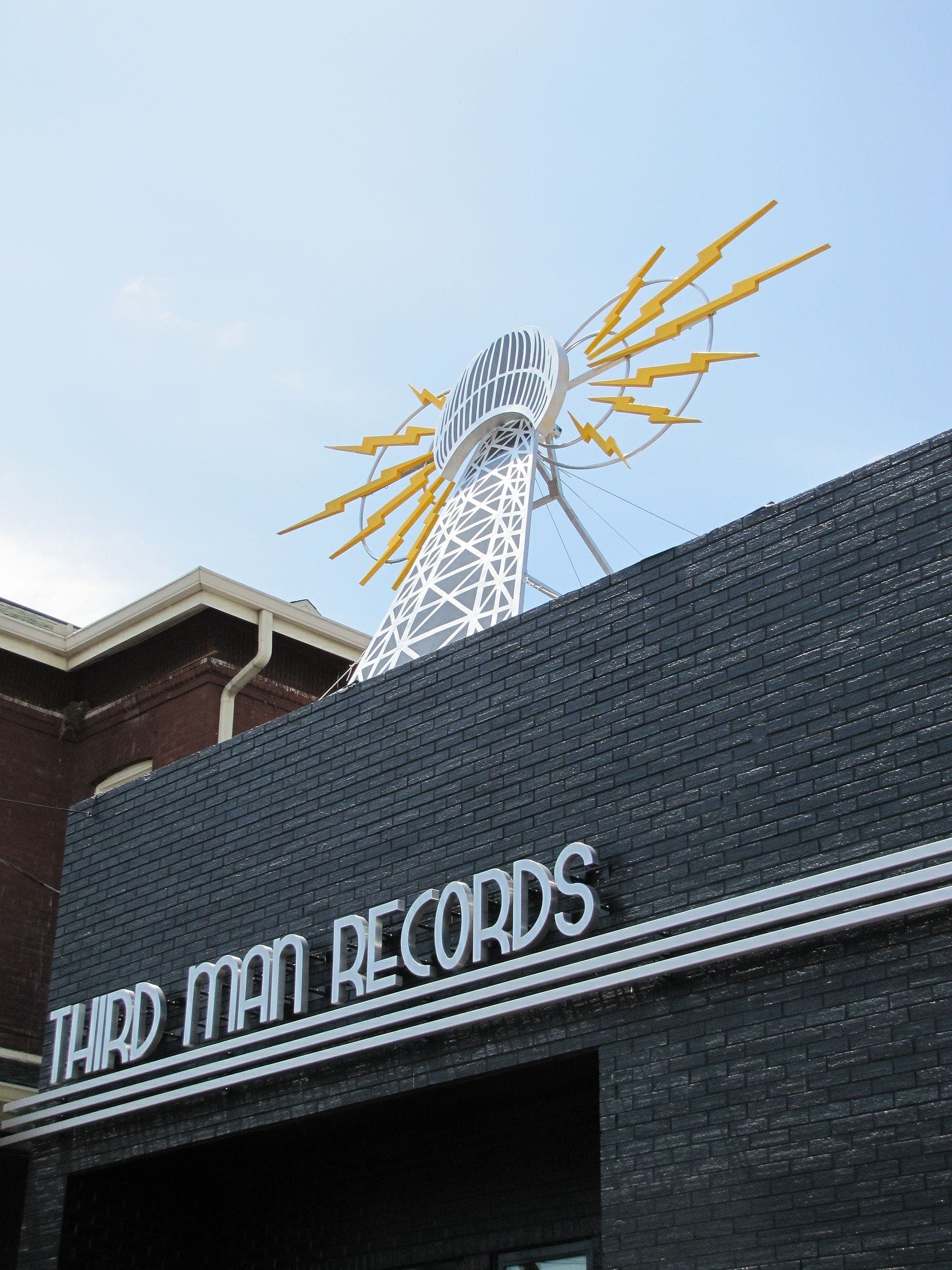 The exterior of Third Man Records in Nashville, featuring a black brick facade and a striking sculpture with yellow lightning bolts against a blue sky.