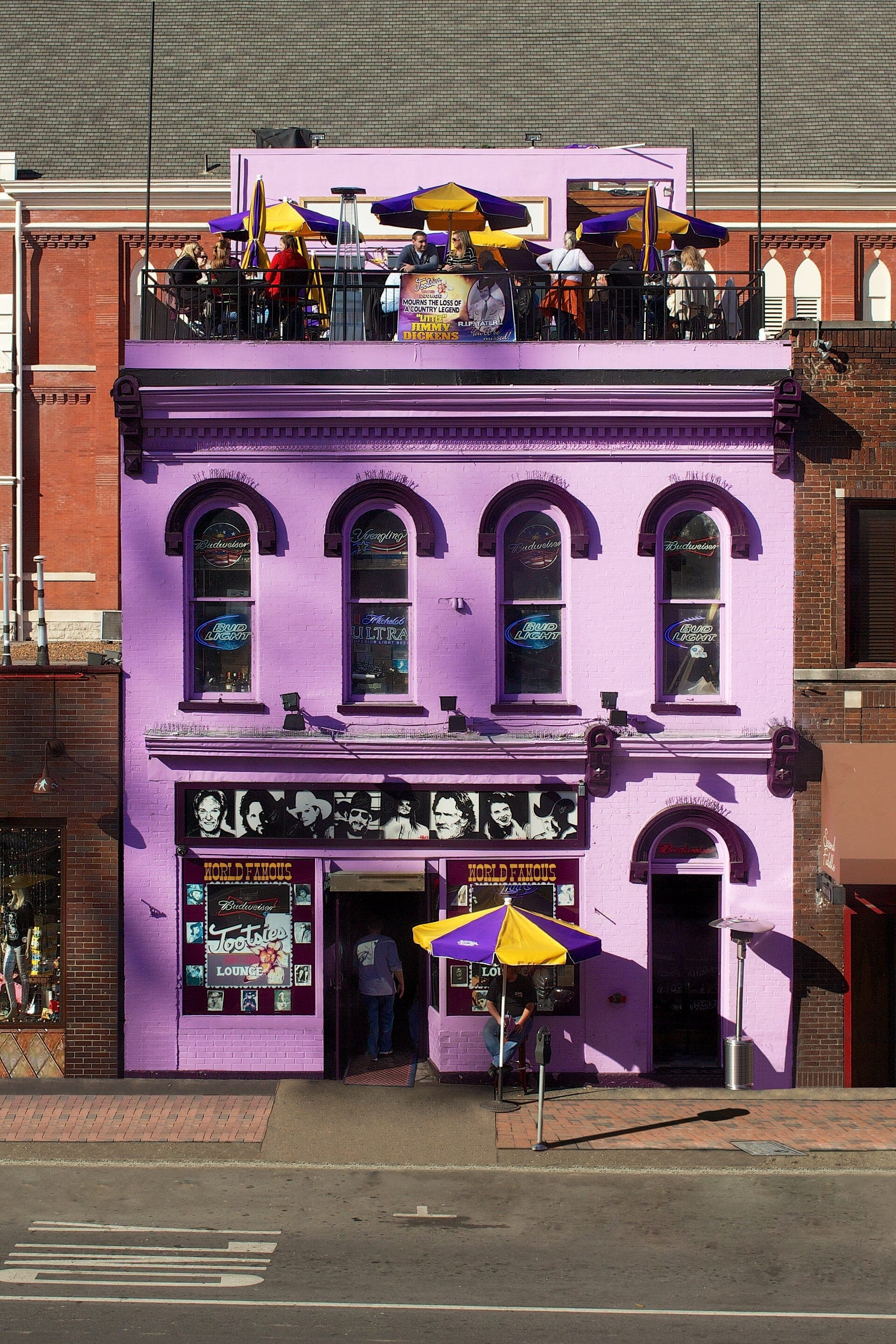 Tootsie's Orchid Lounge with its signature purple facade, bright neon signs, and rooftop patio filled with people under yellow and purple umbrellas.