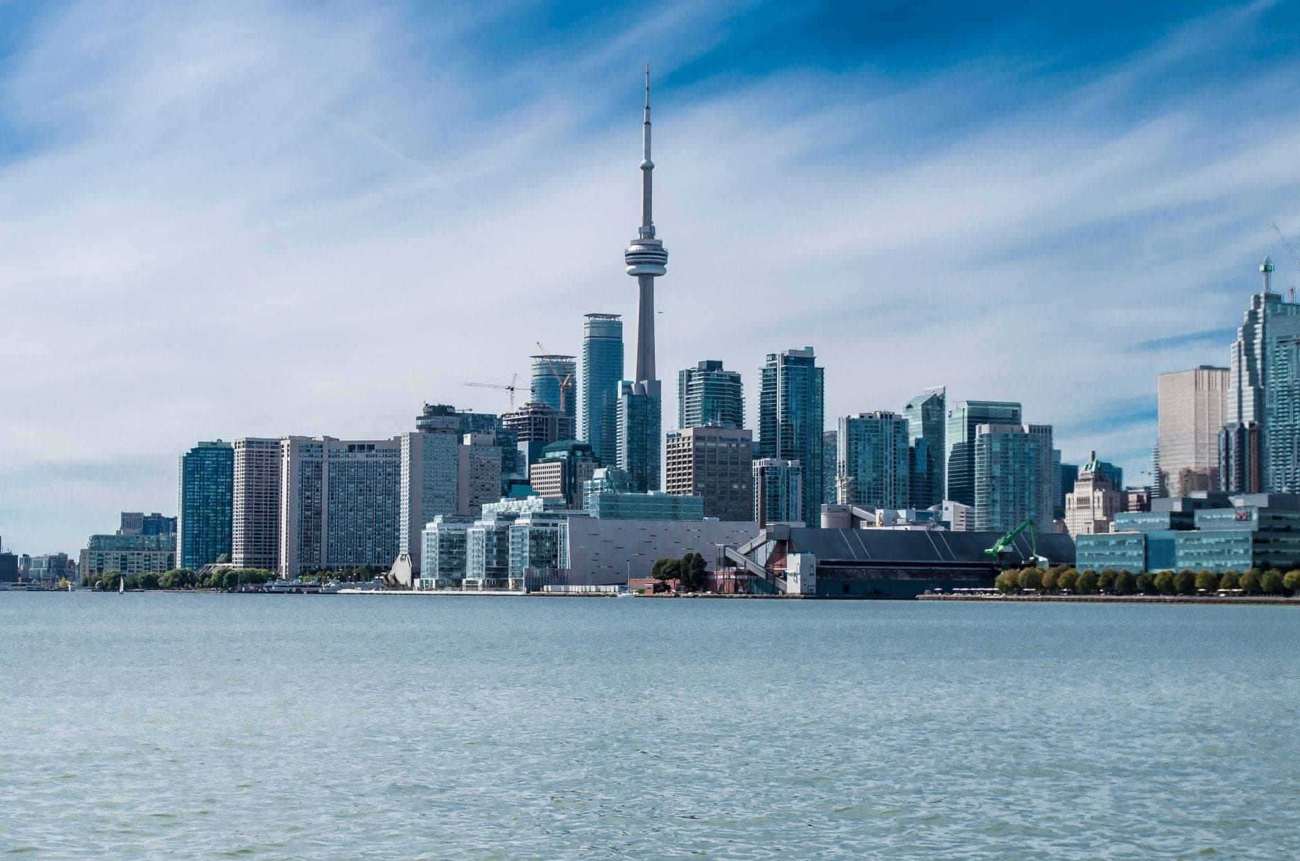 Horizonte de Toronto visto desde el paseo marítimo, con la CN Tower y los rascacielos del centro bajo un cielo azul con nubes tenues.