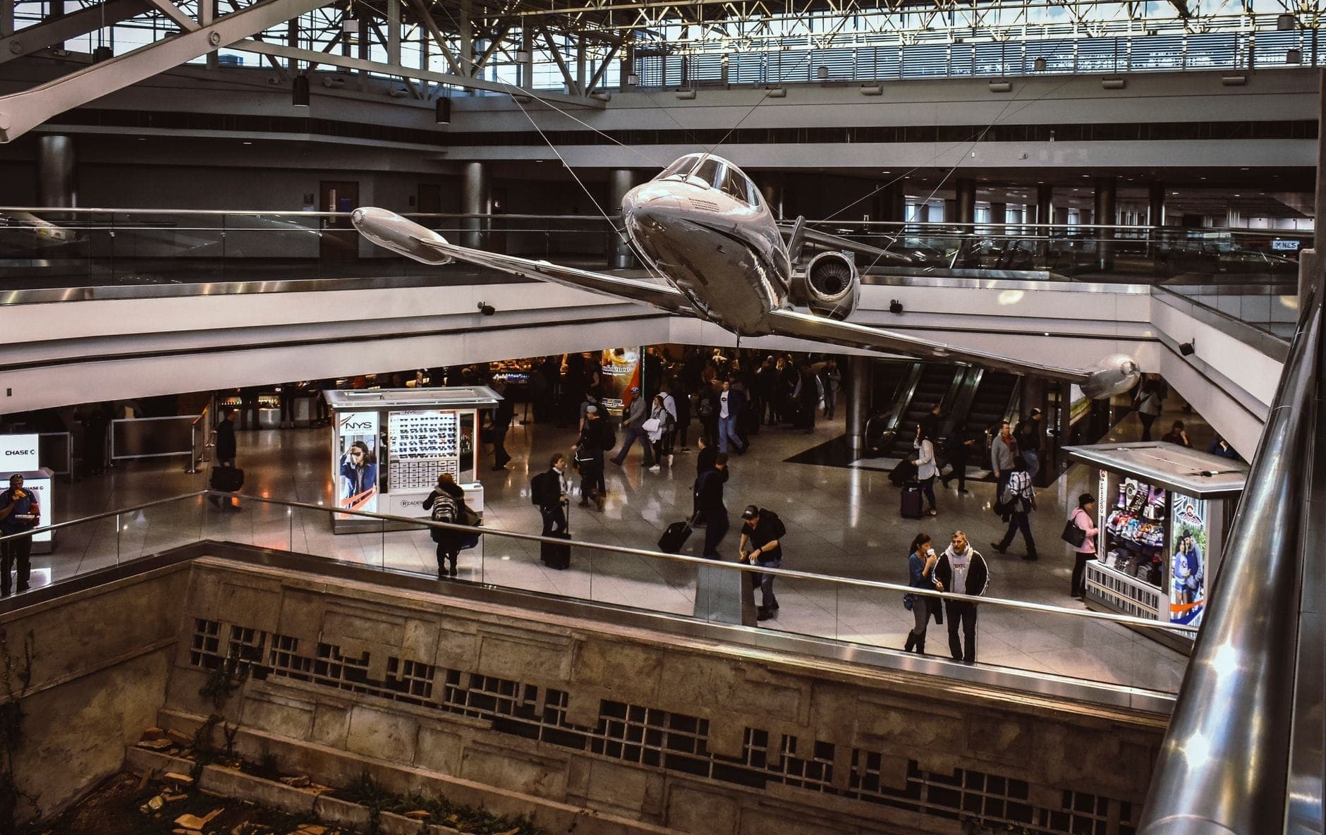 Interno dell'aeroporto Toronto Pearson con una scultura di aereo sospesa e viaggiatori che si muovono in un moderno e vivace terminal.