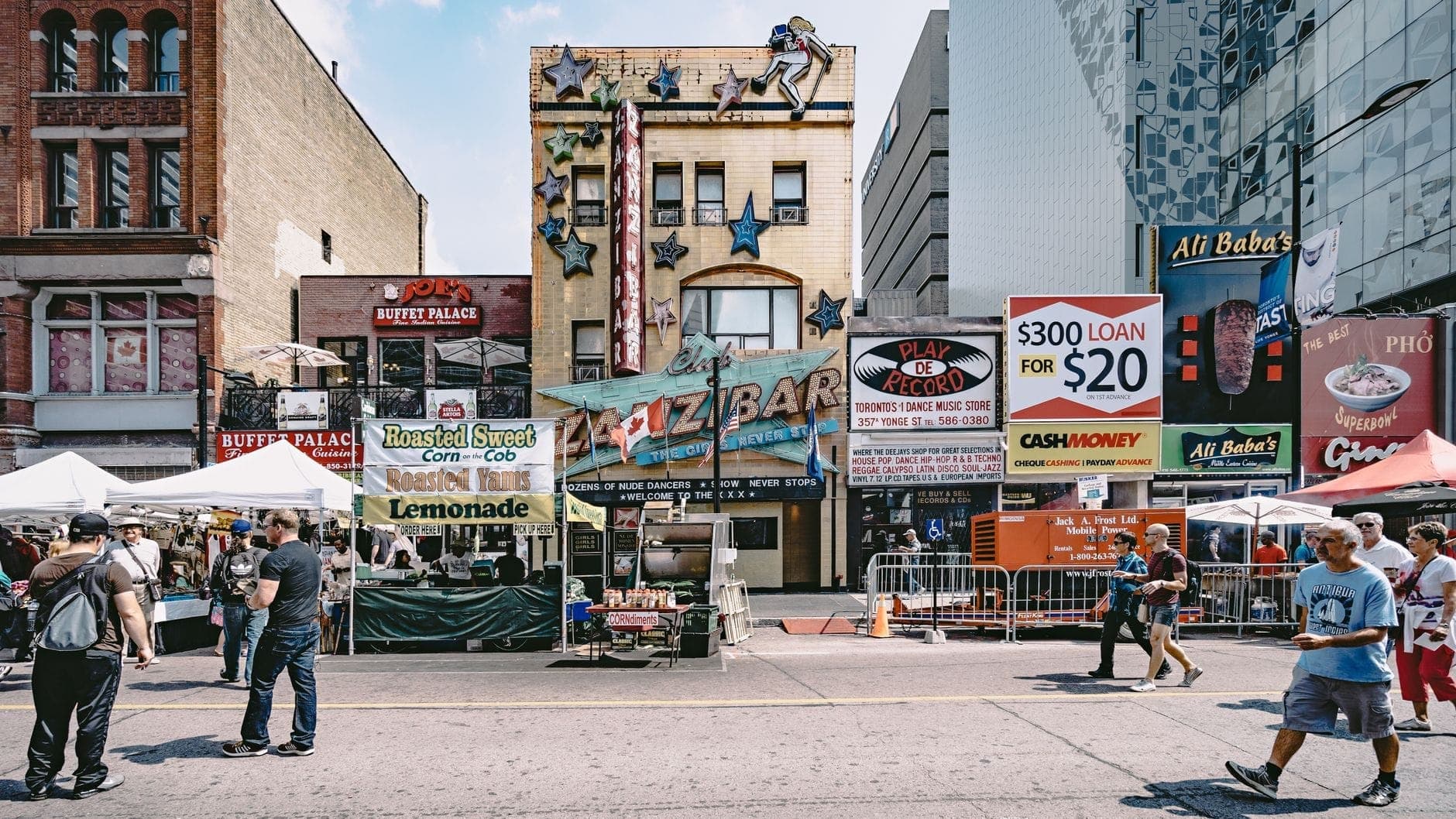 Affollata strada di Toronto fiancheggiata da bancarelle di cibo variegate e ristoranti, insegne colorate e persone che camminano, che evoca l'atmosfera vivace di un corridoio gastronomico.
