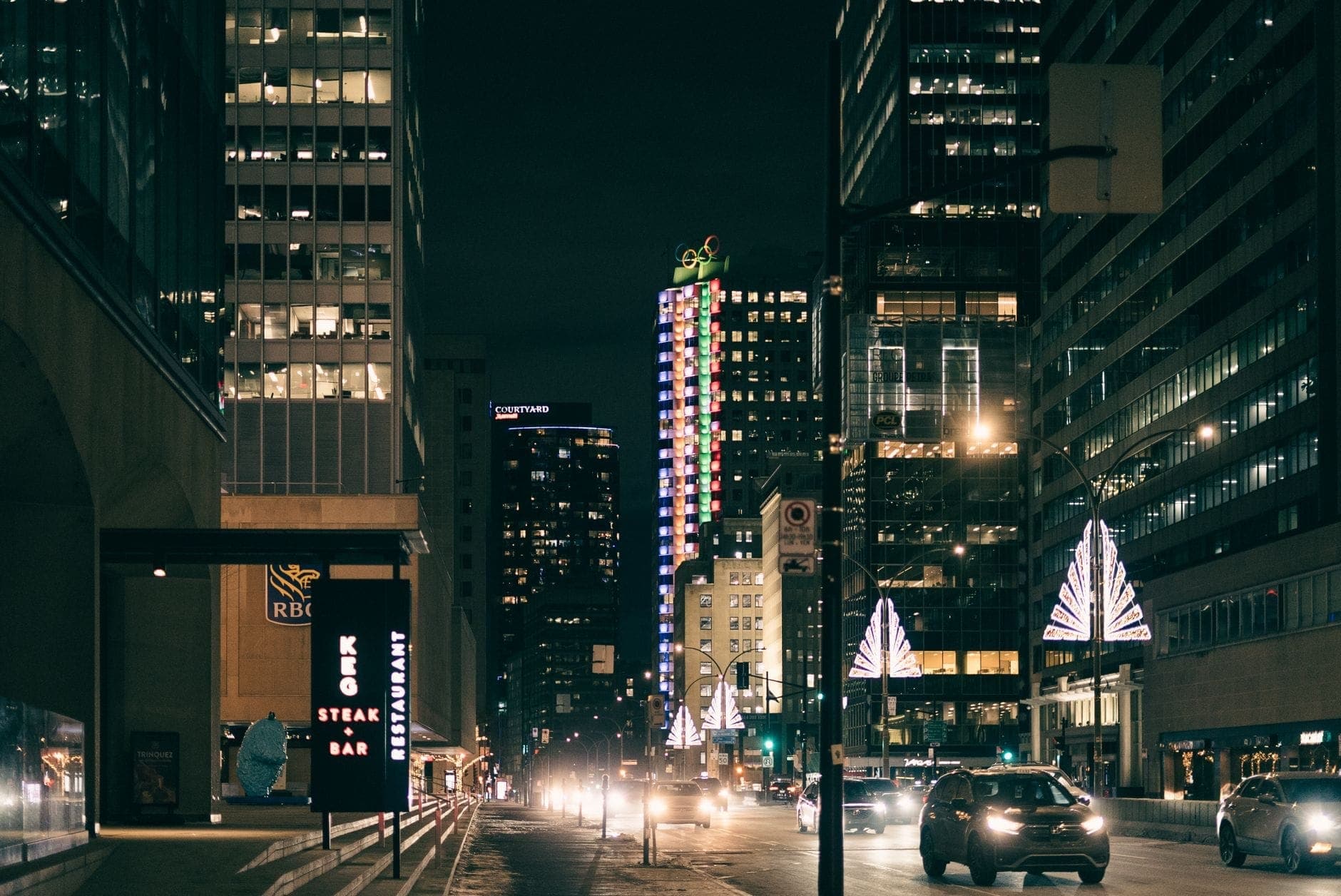 Vista notturna del centro di Toronto con grattacieli illuminati, automobili e un'insegna del The Keg Steakhouse, che suggerisce una cena raffinata in città.