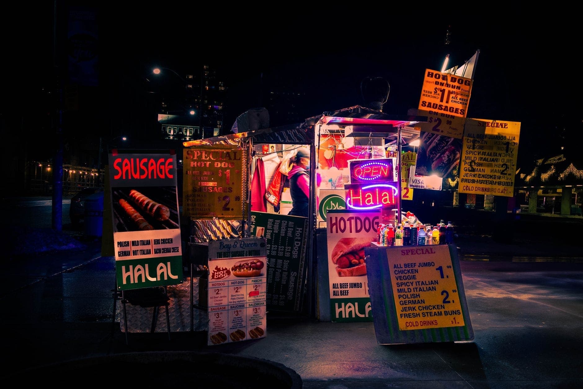 Un vivace stand di street food con hot dog e salsicce halal a Toronto di notte, brillantemente illuminato con insegne al neon e menu variegati.