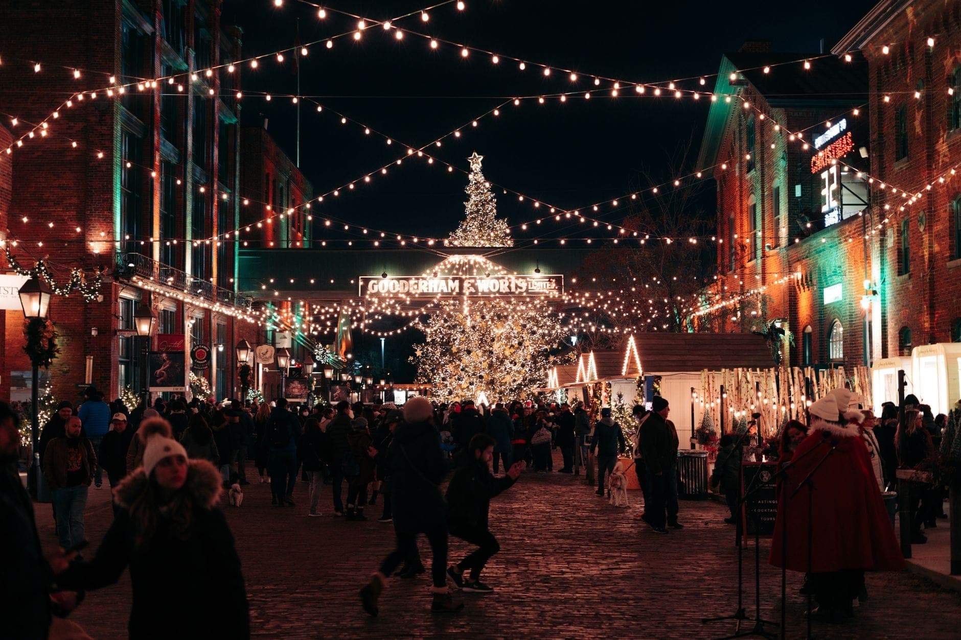 Multitudes disfrutan de una noche invernal festiva en el Distillery District de Toronto, con luces, puestos de mercado y un gran árbol de Navidad.