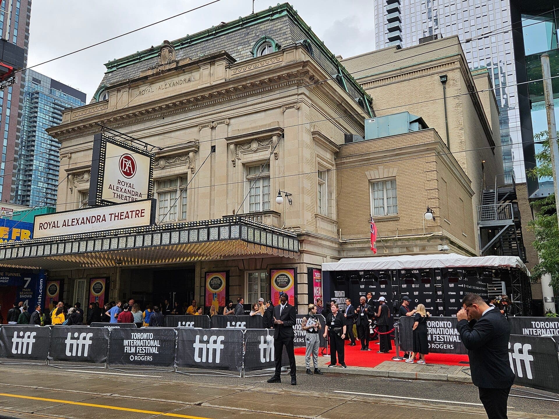 Kerumunan berkumpul di luar Royal Alexandra Theatre bersejarah di Toronto selama Toronto International Film Festival, dengan papan tanda festival dan karpet merah.