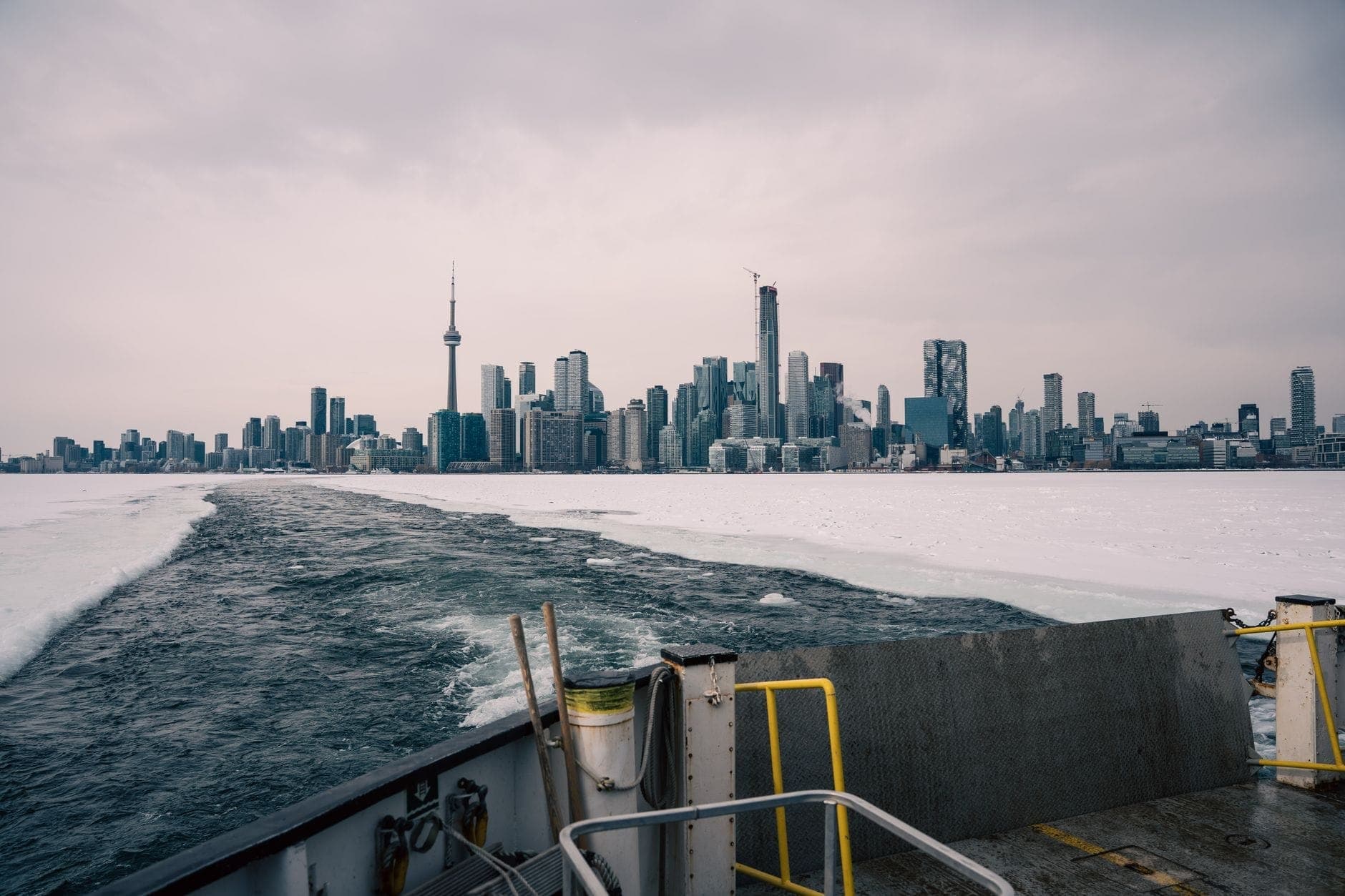 View from ferry with Toronto skyline in winter, showing ice on the lake and cloudy sky, highlighting off-season conditions.