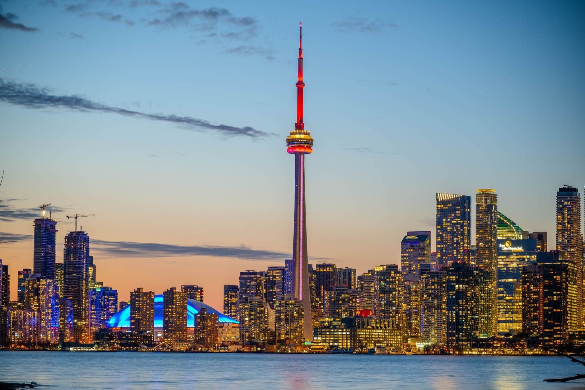 Atardecer sobre el horizonte de Toronto con la CN Tower y lujosos rascacielos iluminados, vistos desde el paseo marítimo.