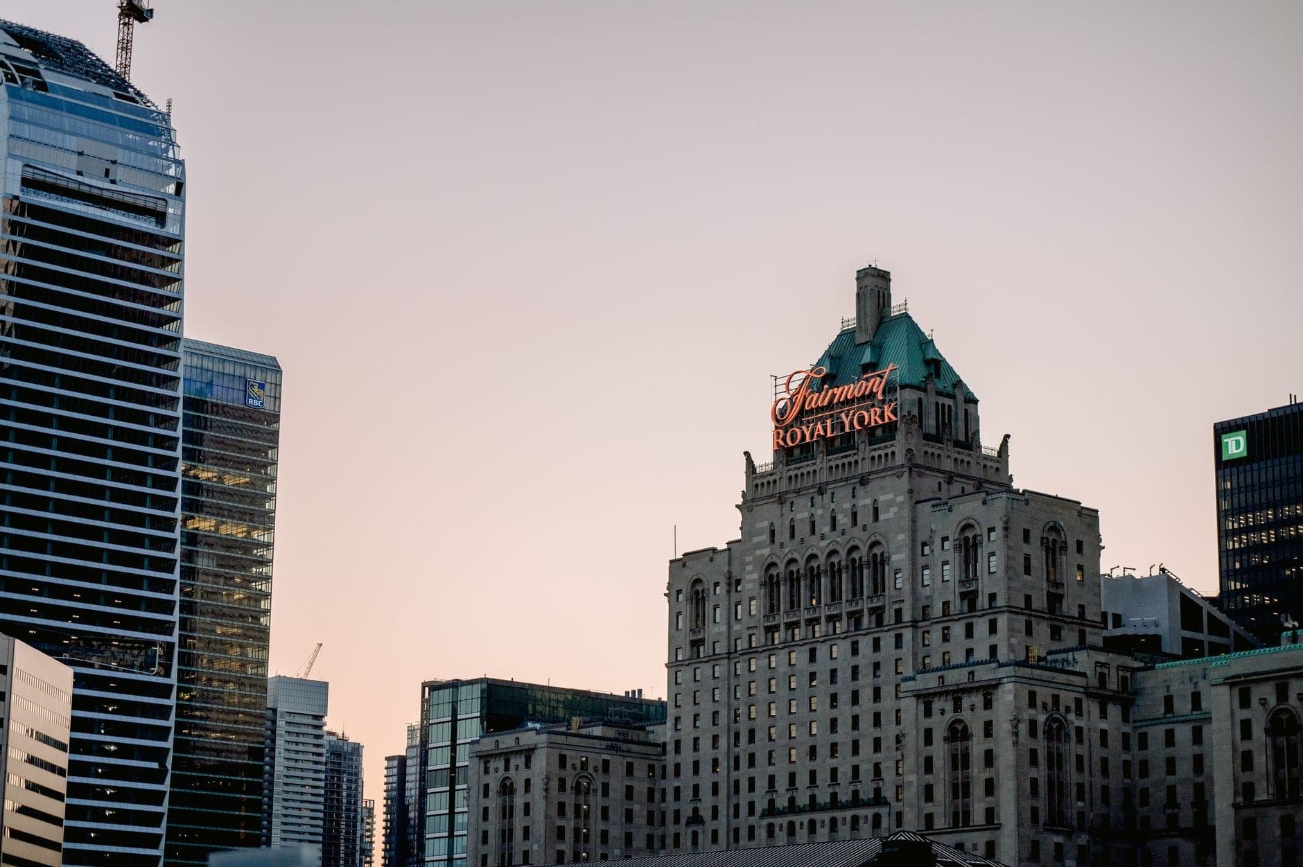 El histórico hotel Fairmont Royal York con su iluminado letrero rojo entre los rascacielos del centro de Toronto al atardecer.