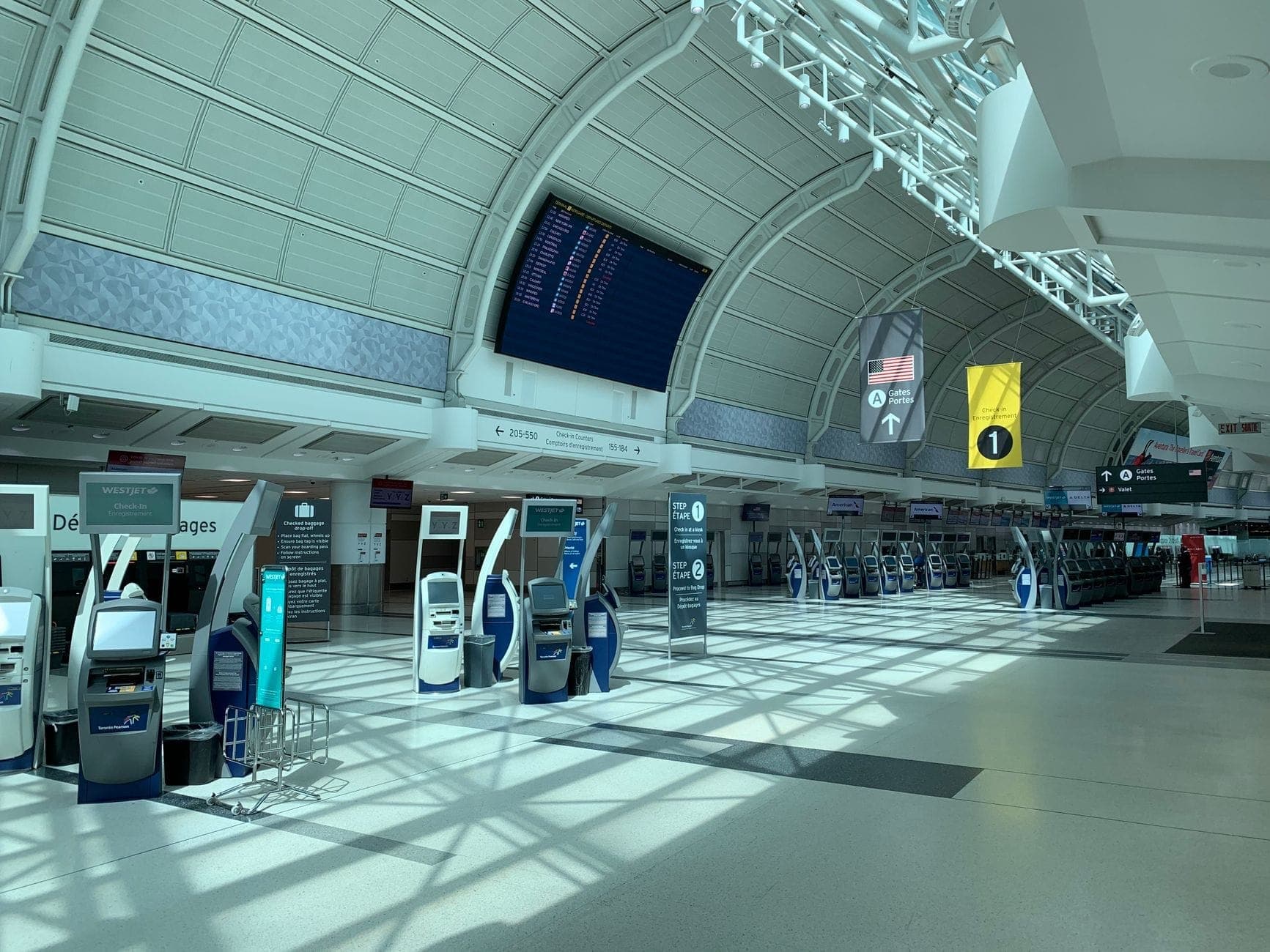 Interior de la terminal del Aeropuerto Internacional Toronto Pearson con quioscos de auto-facturación y pantallas de salidas en una amplia sala iluminada por el sol.