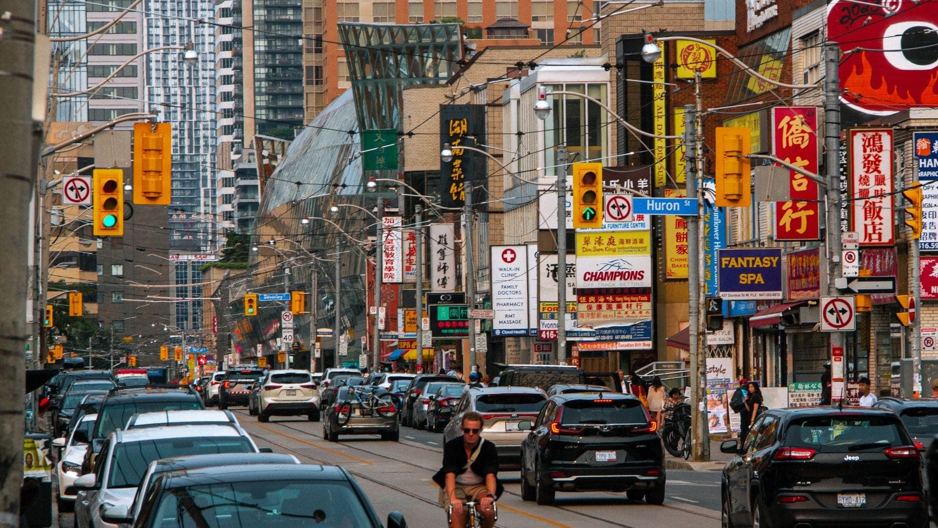 Vivace scena di strada nel Chinatown di Toronto con insegne cinesi, negozi, ristoranti, auto e un ciclista, alti edifici sullo sfondo.