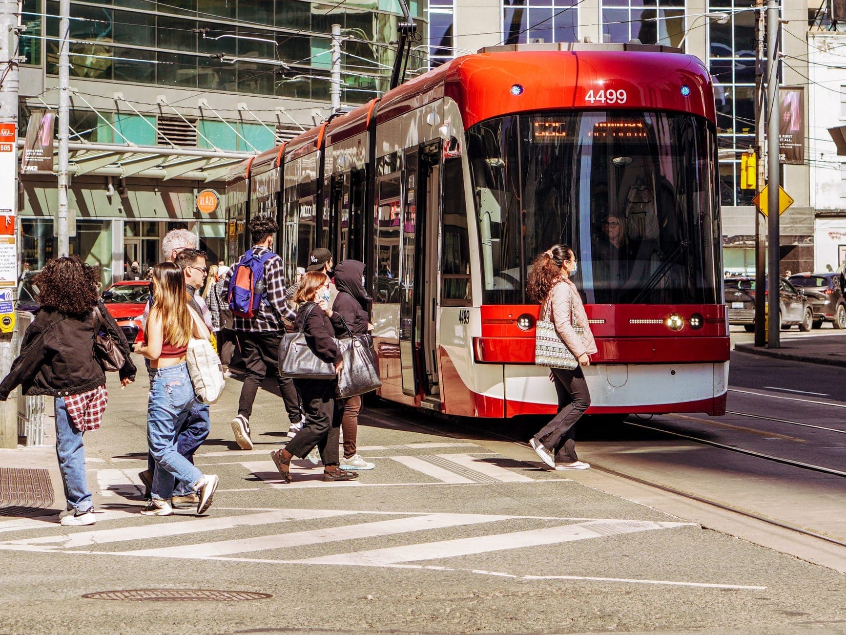 Persone che attraversano la strada davanti a un moderno tram rosso e bianco di Toronto a un incrocio cittadino di giorno.