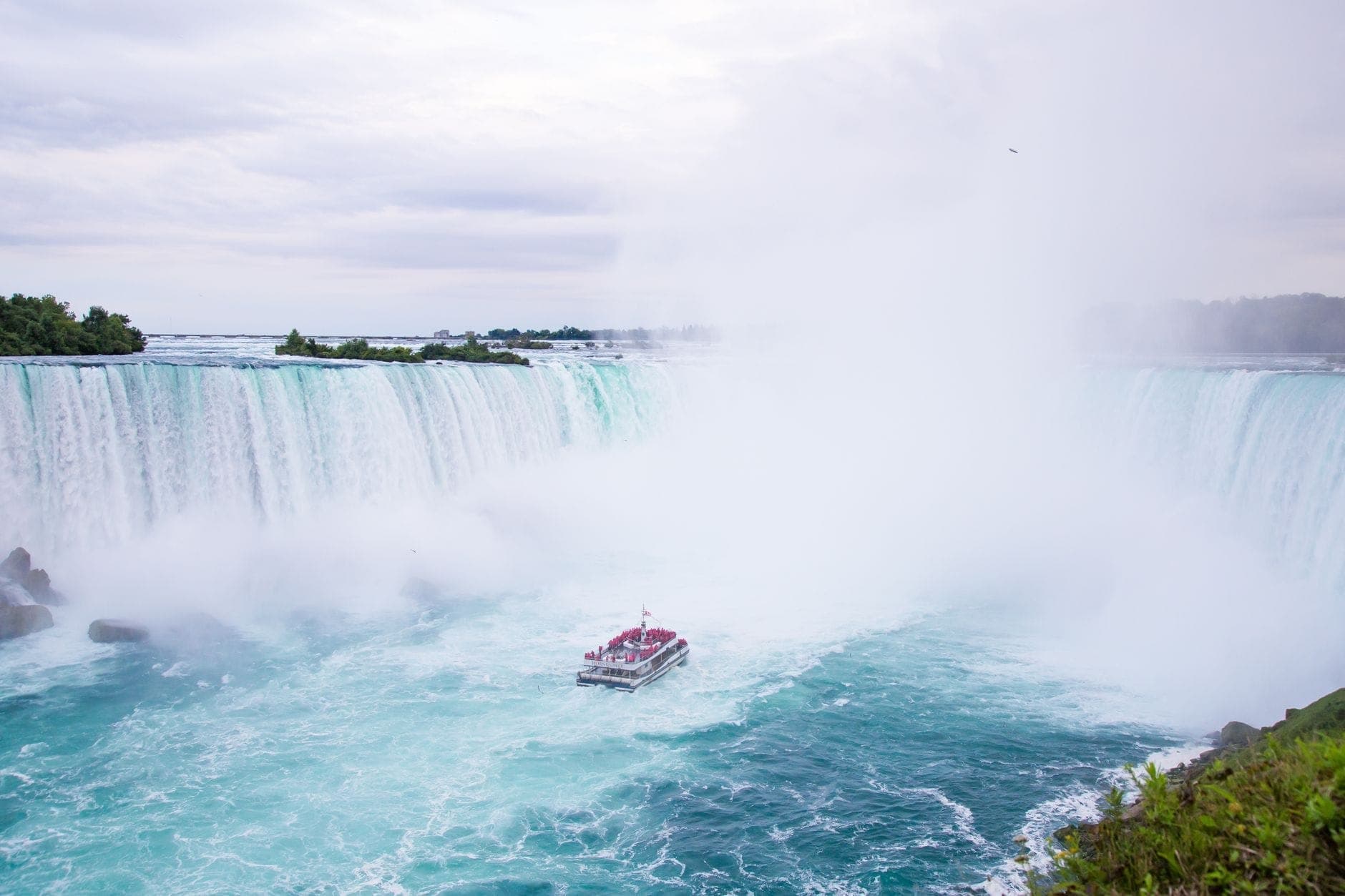 Un barco turístico se acerca a la base de las Cataratas del Niágara, rodeado de niebla y las poderosas cascadas al fondo.