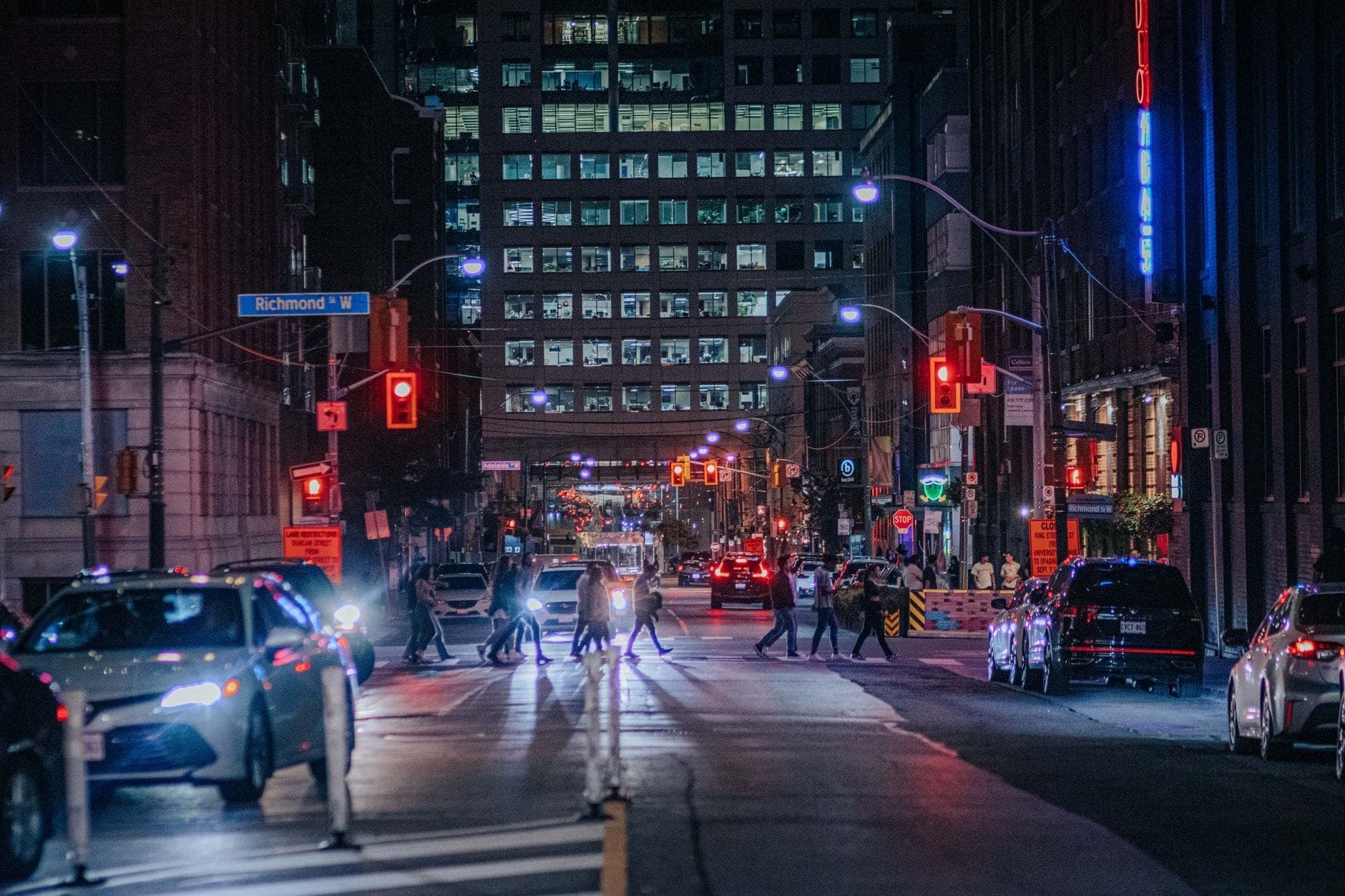 Vista nocturna de una concurrida calle del centro de Toronto cerca de Richmond Street, peatones cruzando, autos, luces de la ciudad y edificios.