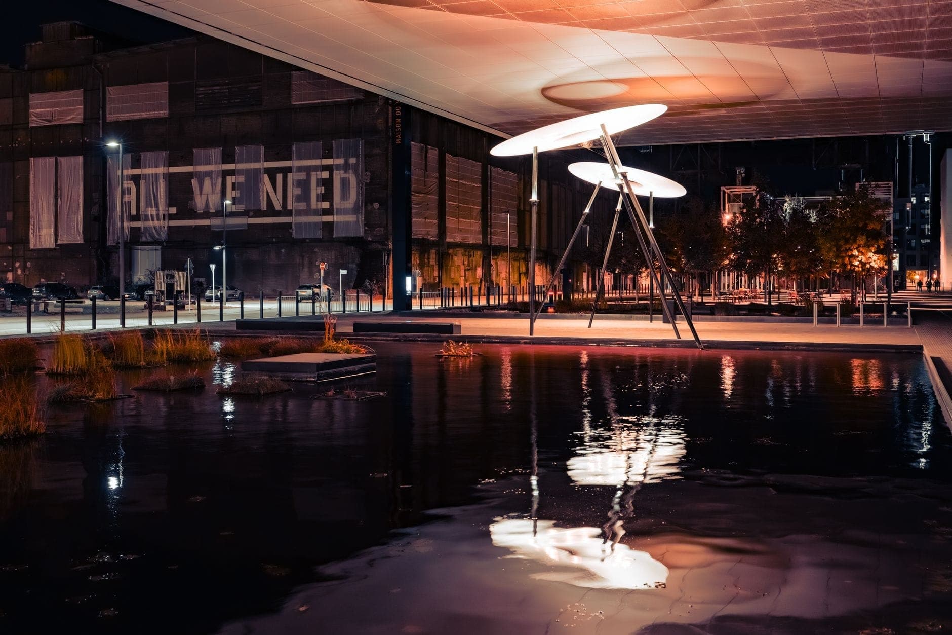 Installazione artistica notturna all'aperto con grandi strutture circolari illuminate sull'acqua, contesto urbano moderno ed edifici sullo sfondo a Toronto.