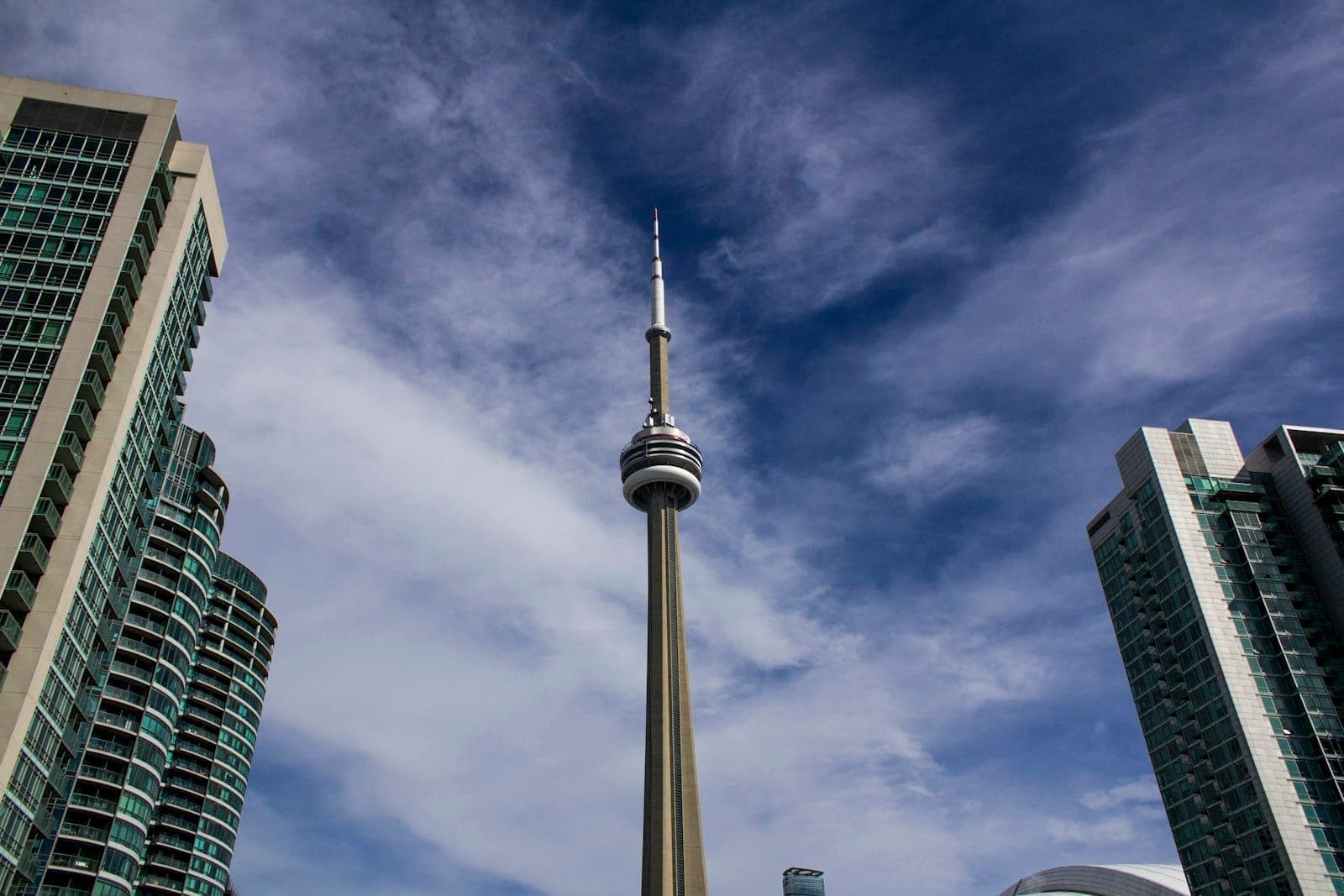 Skyline di Toronto con la CN Tower e moderni grattacieli sotto un cielo parzialmente nuvoloso.