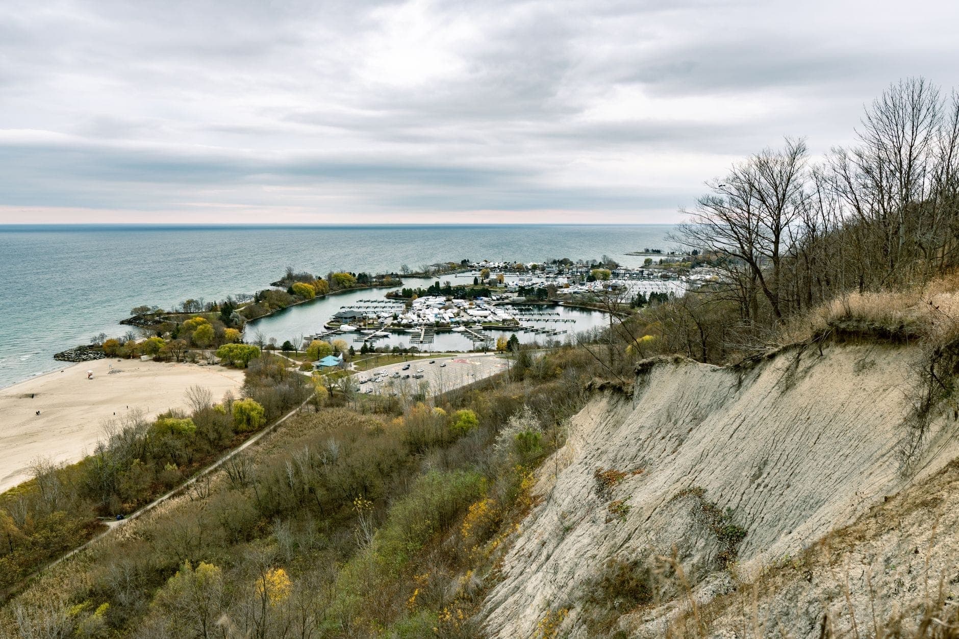 Vista degli Scarborough Bluffs di Toronto con scogliere frastagliate, burrone boscoso, spiaggia sabbiosa e la riva del lago Ontario sotto un cielo nuvoloso.